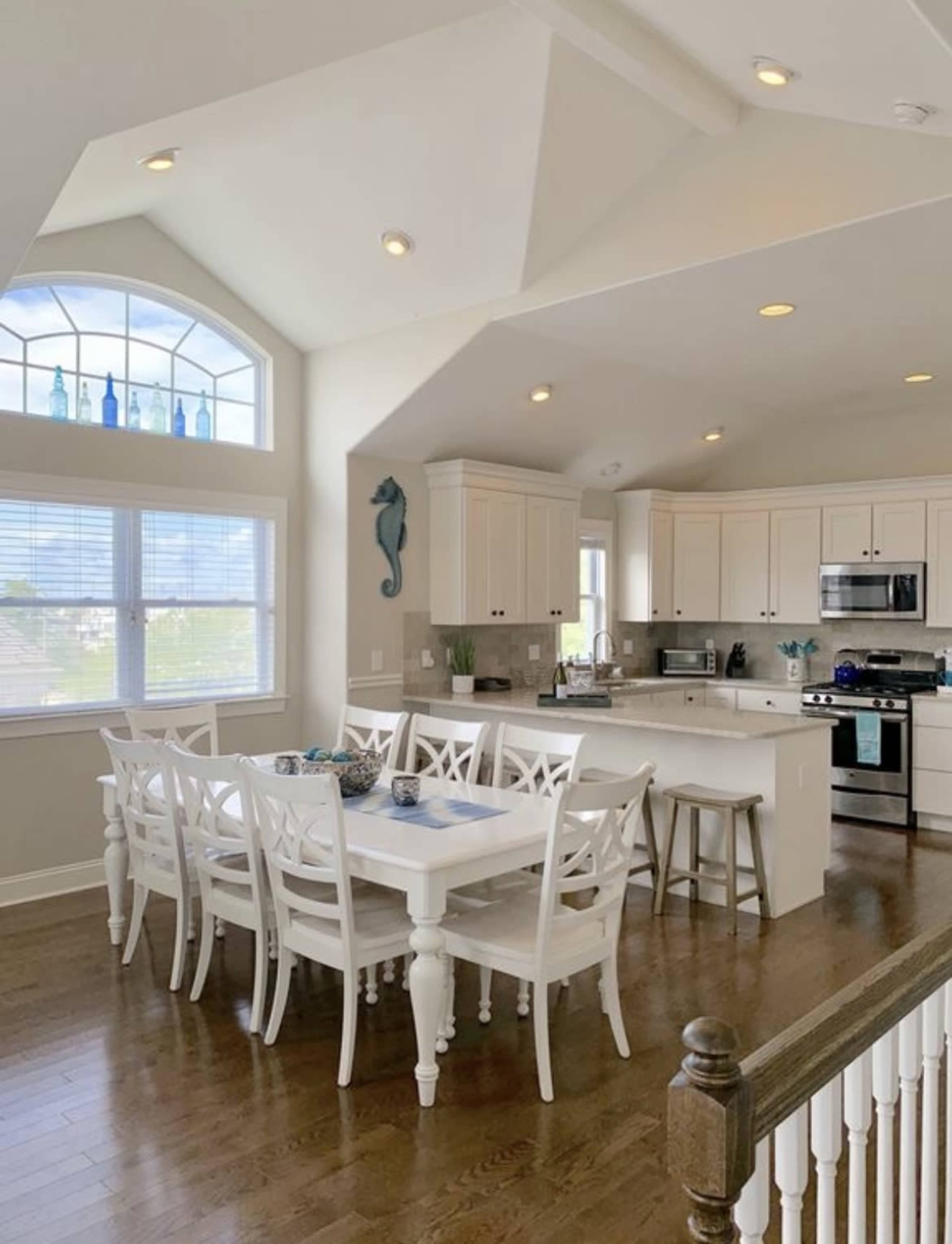 A bright kitchen features white cabinets, a dining table with chairs, and large windows letting in natural light.