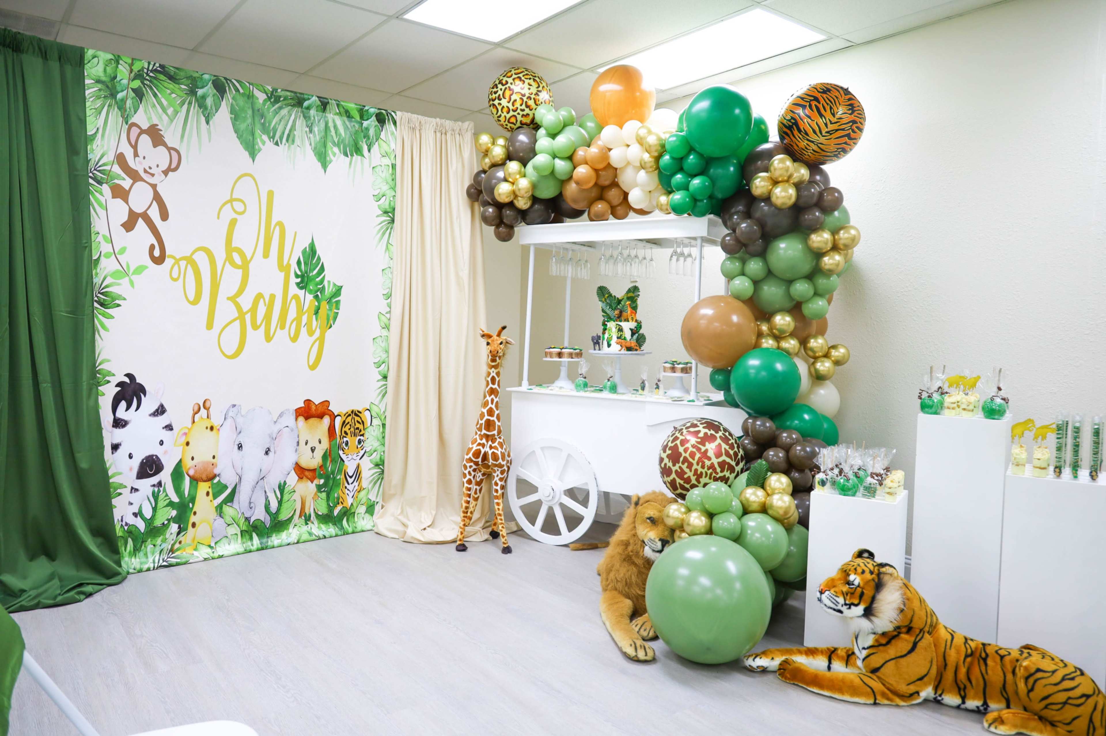 The scene features a decorated room for a baby shower, with a green and animal-themed backdrop, a balloon arch, and stuffed animal decorations including a lion and a tiger.