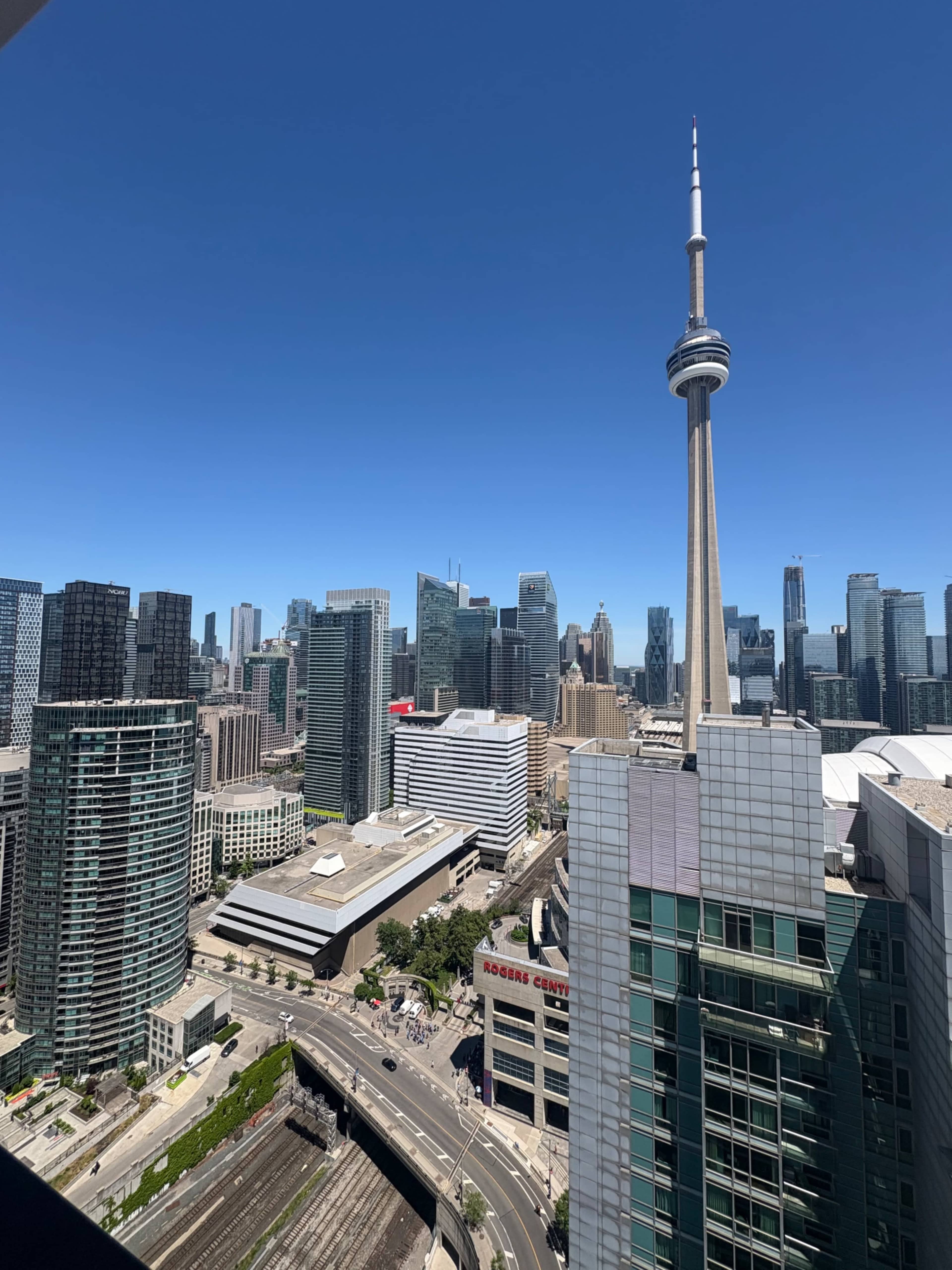 The image shows a clear view of downtown Toronto, featuring the CN Tower and a mix of modern skyscrapers against a blue sky.