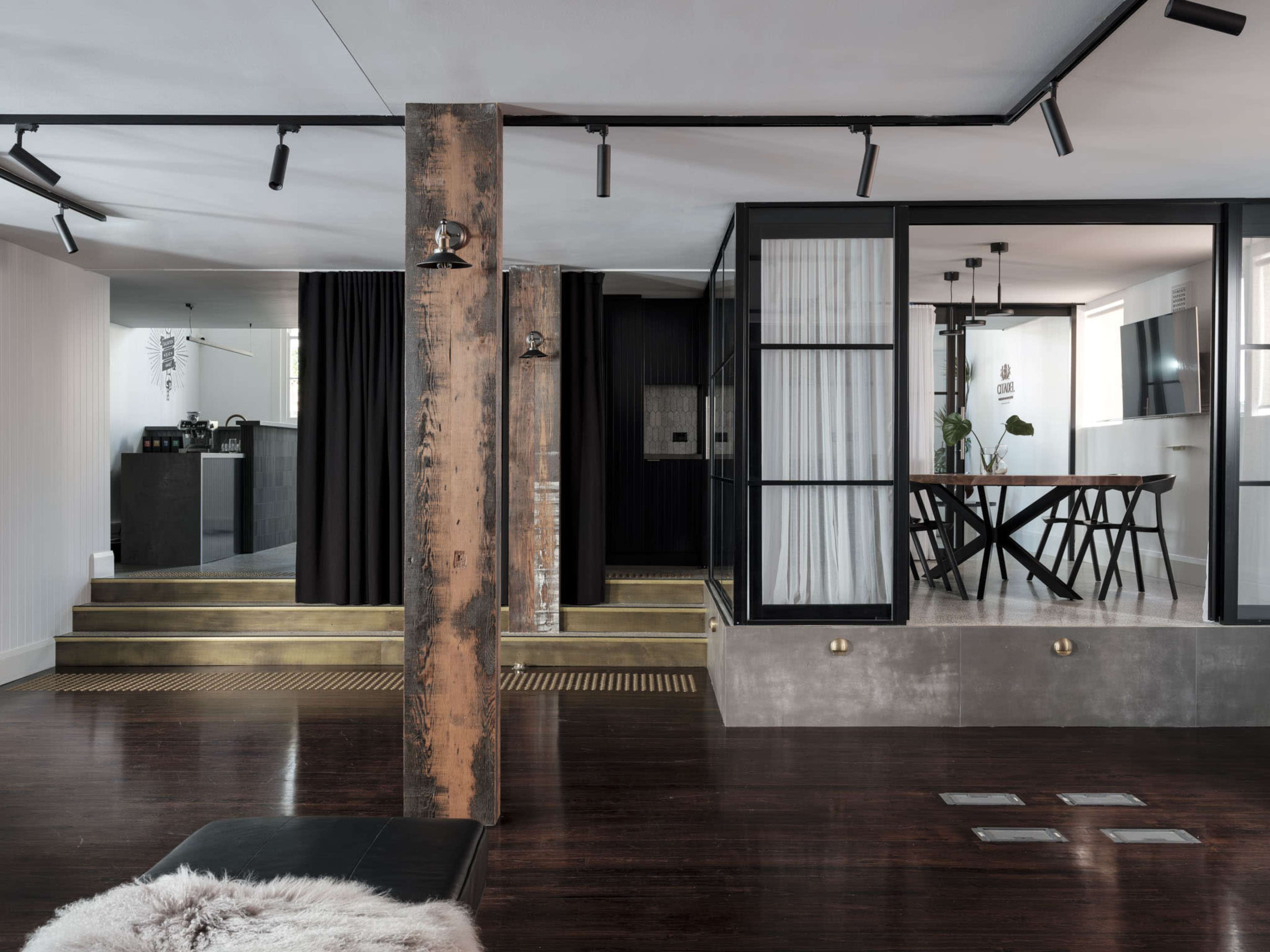 The image shows a modern interior space featuring a combination of wooden floors, black curtains, glass partitions, and an industrial-style support column.