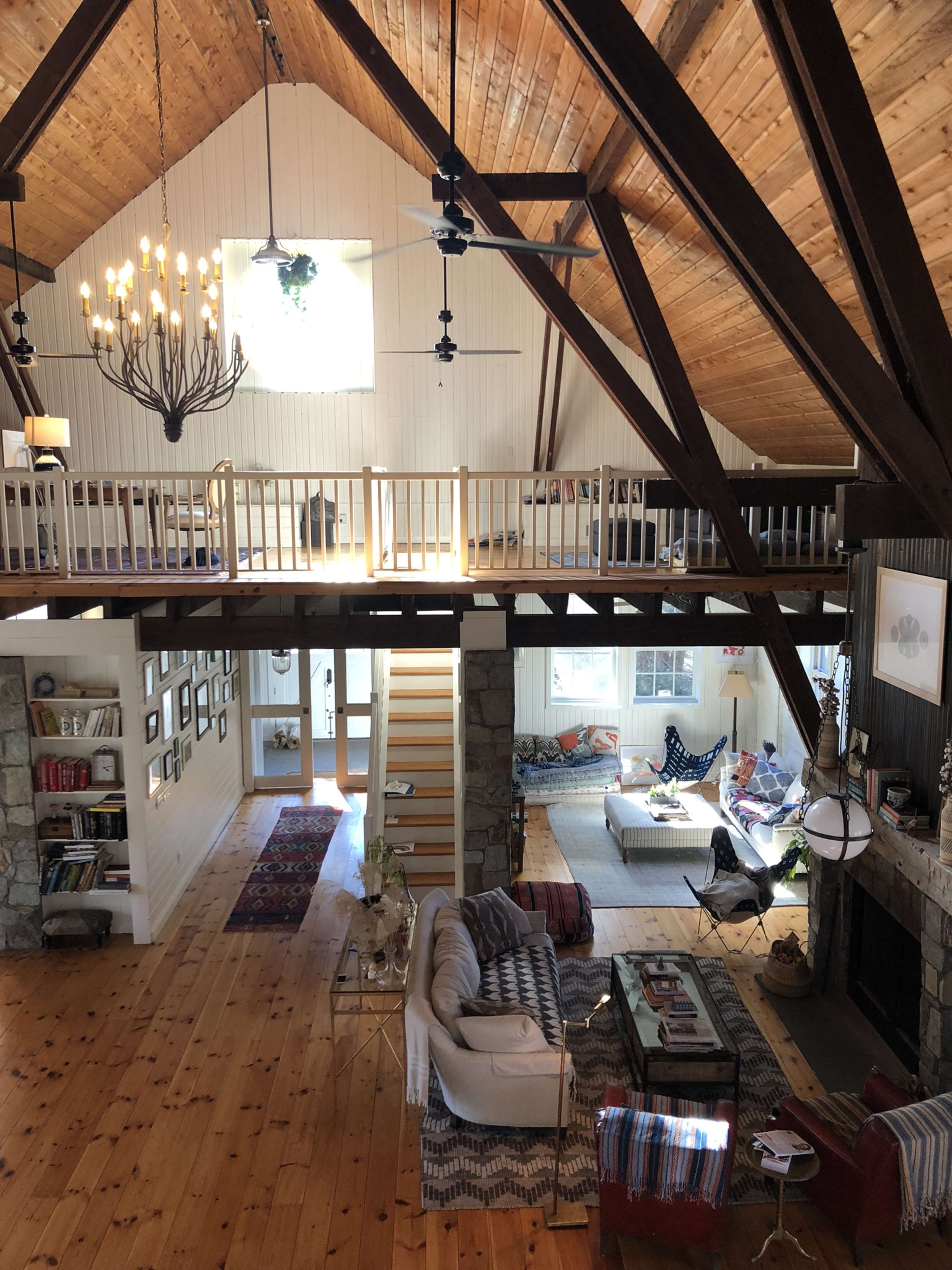 A spacious living room with high wooden beams, a lofted area, and a cozy seating arrangement near a fireplace.