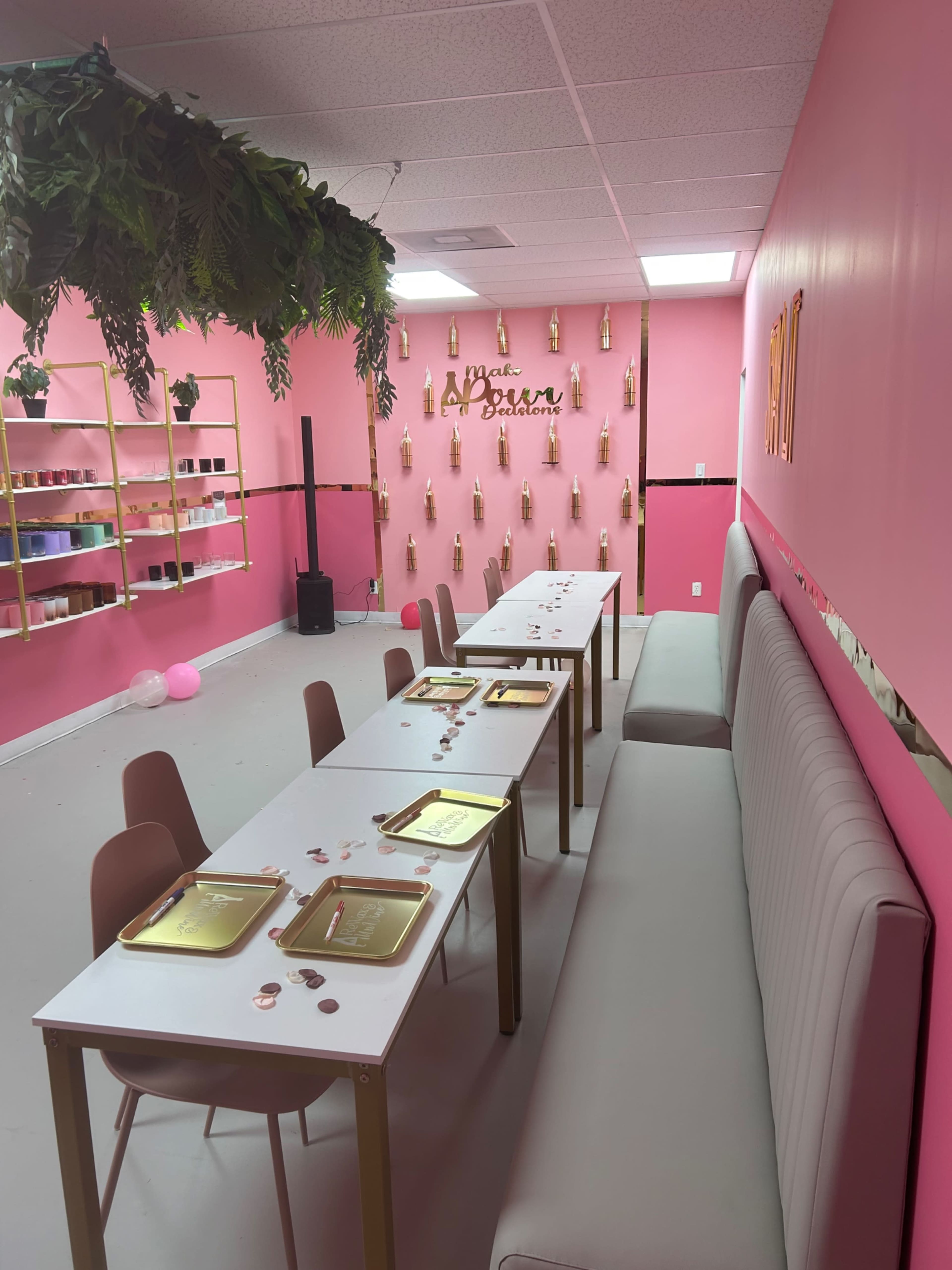The image shows a brightly decorated room with pink walls, two long tables set for a gathering, and gold plates arranged on the tables amidst decorative elements.