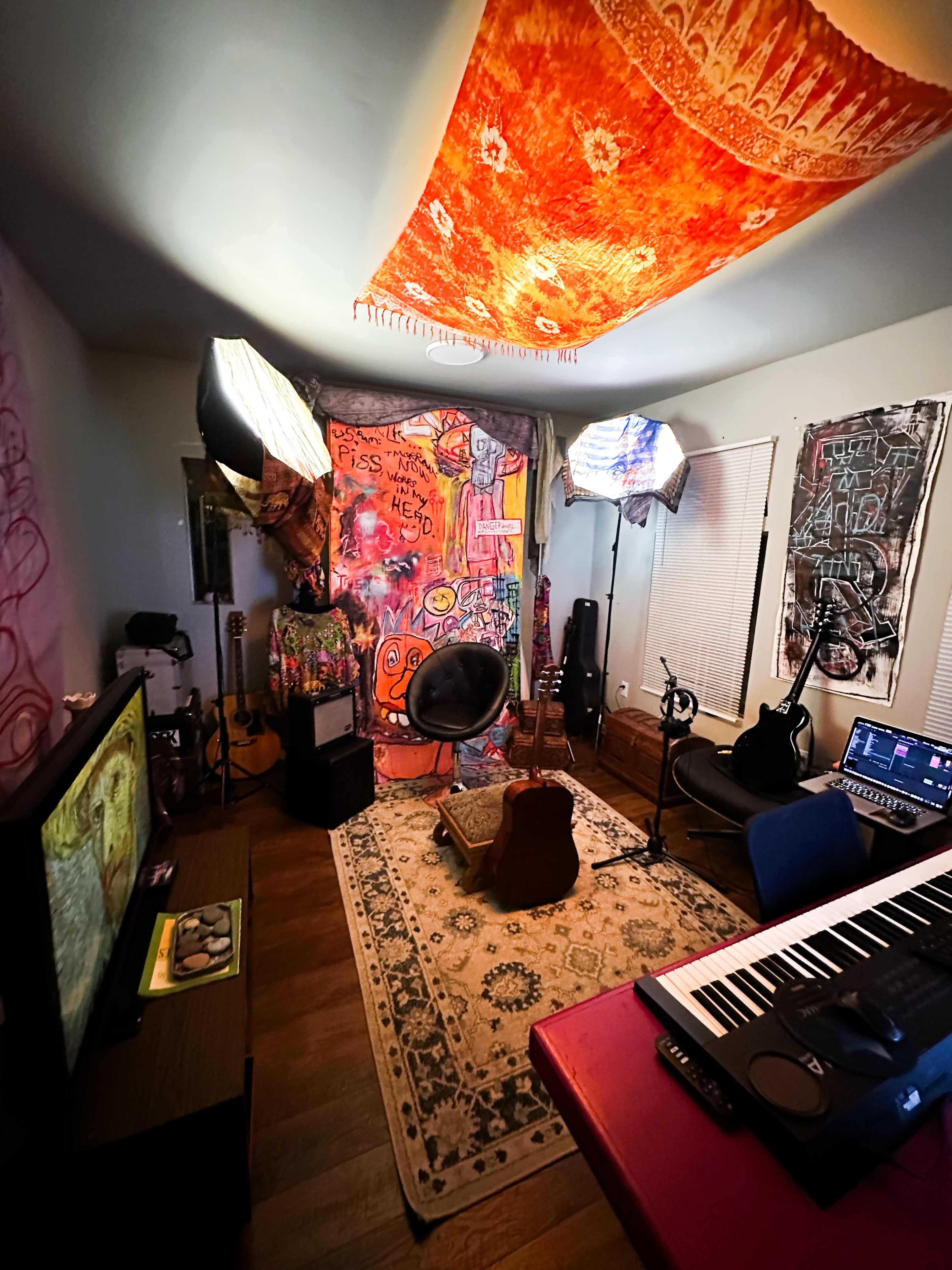 A cozy music studio features a colorful tapestry, musical instruments, and professional lighting setup, creating an artistic atmosphere.