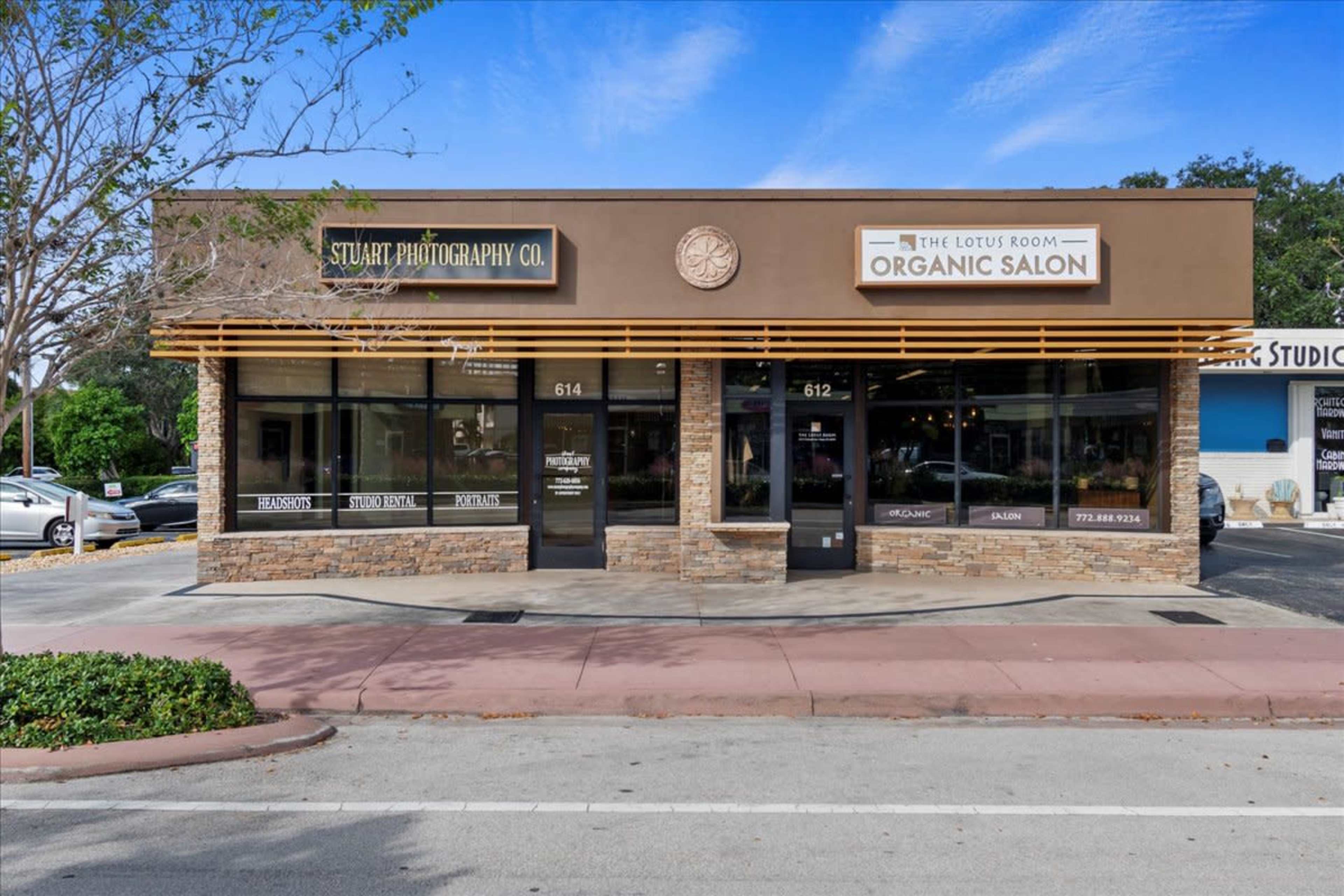 A single-story commercial building featuring two storefronts, one labeled "Stuart Photography Co." and the other "The Lotus Room Organic Salon," with a landscaped area in front.