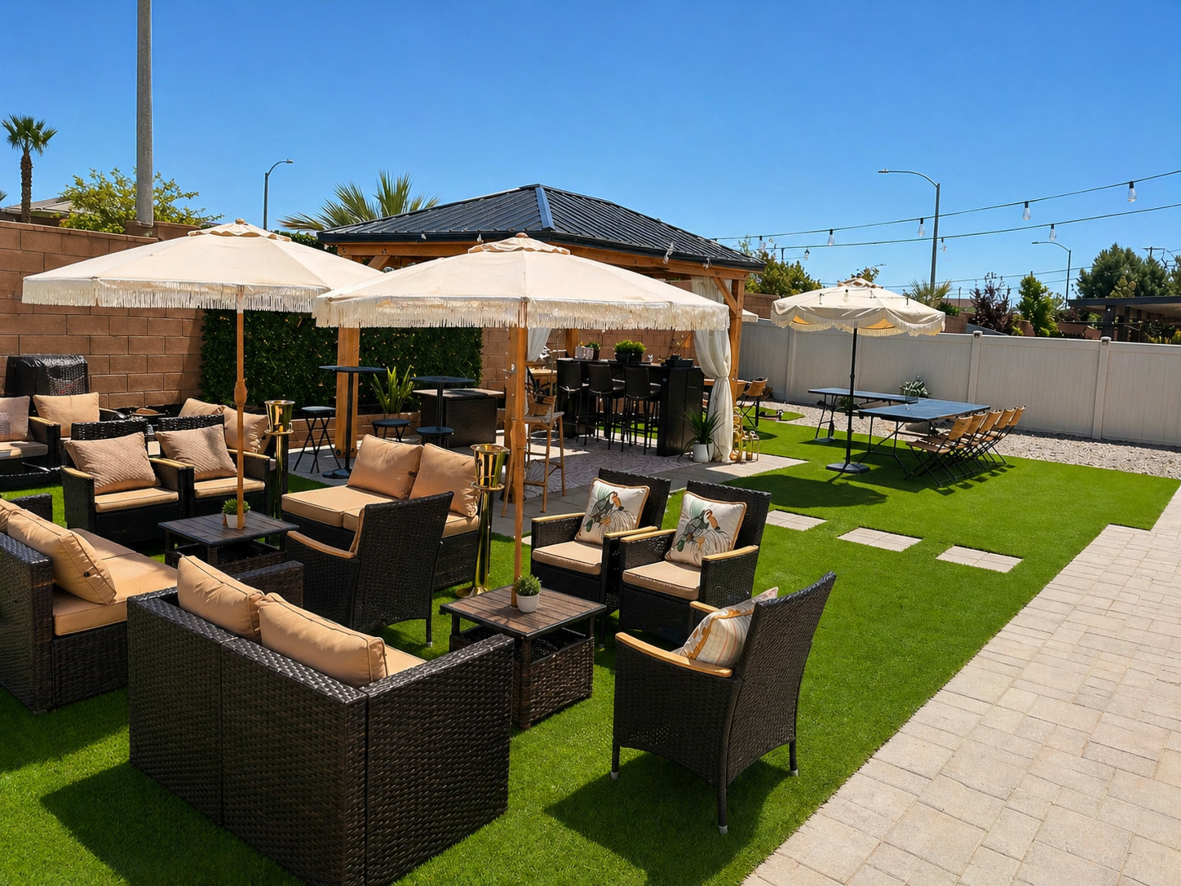 The image shows a landscaped outdoor patio area featuring wicker seating, umbrellas, and a dining space with a pergola in the background.