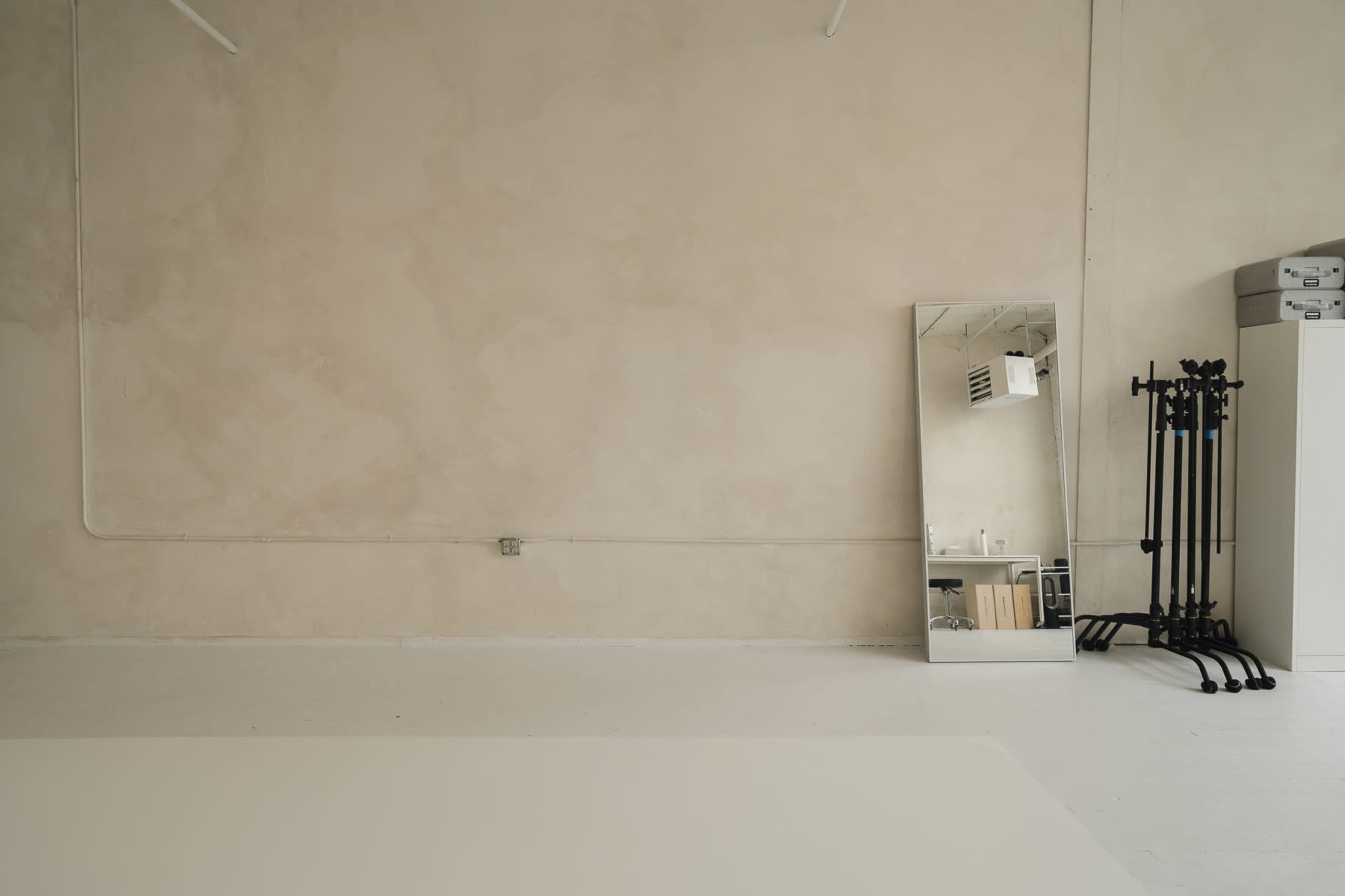 An empty room features a large mirror against a textured wall, with a few black stands and storage boxes in the corner.