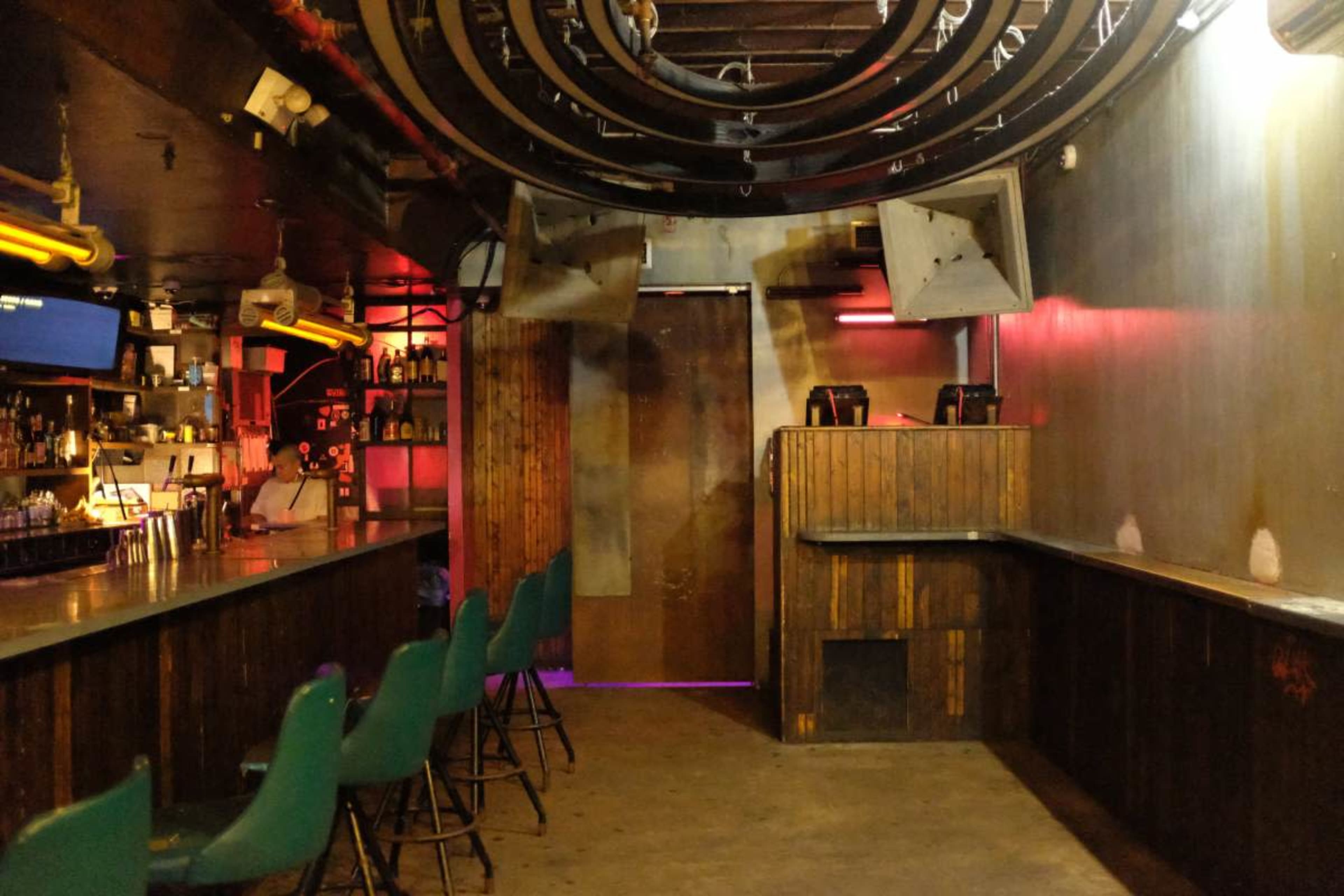 The image shows an empty bar with a long counter, green stools, and dim lighting.