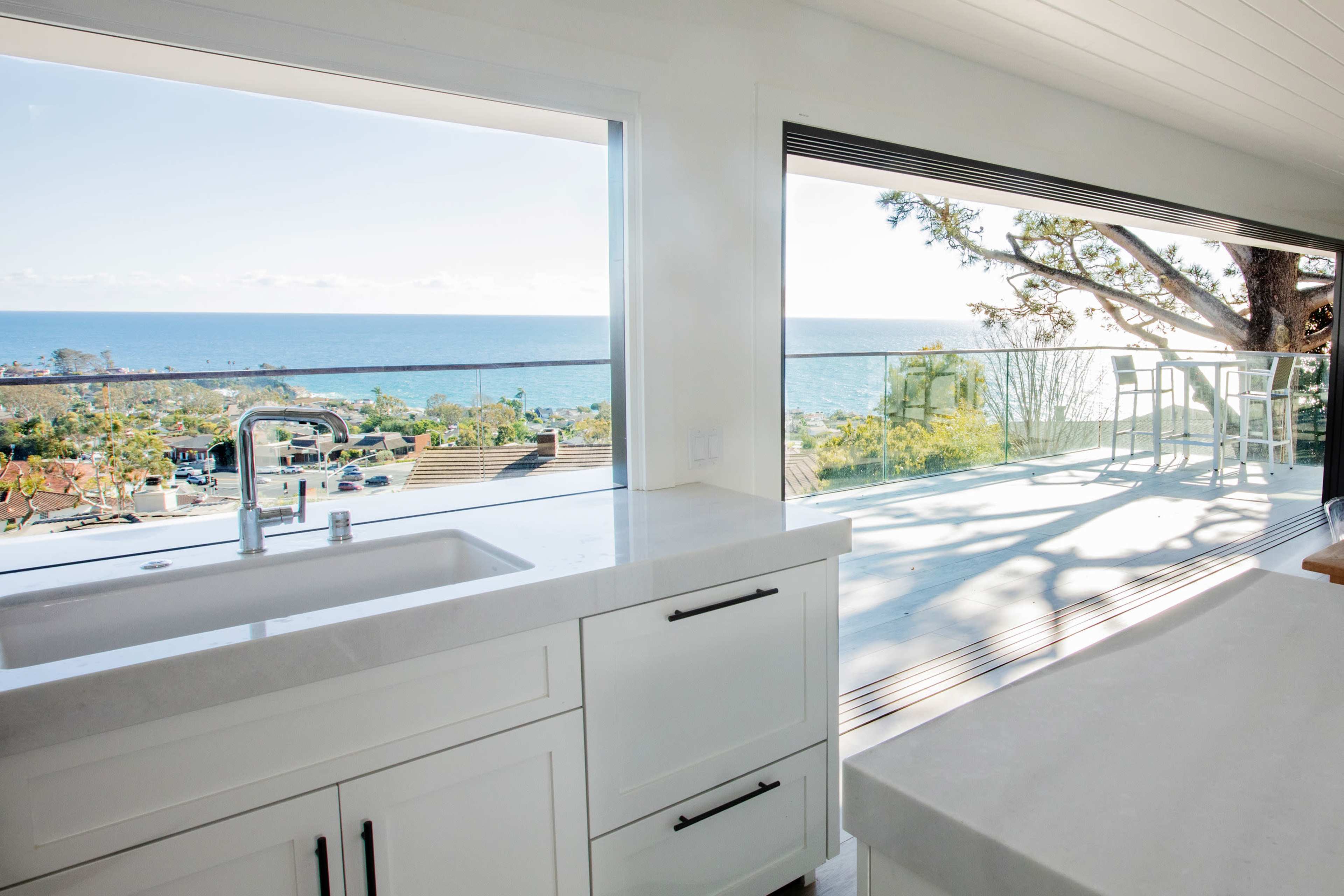 A modern kitchen features a large window that offers a view of the ocean and a balcony.