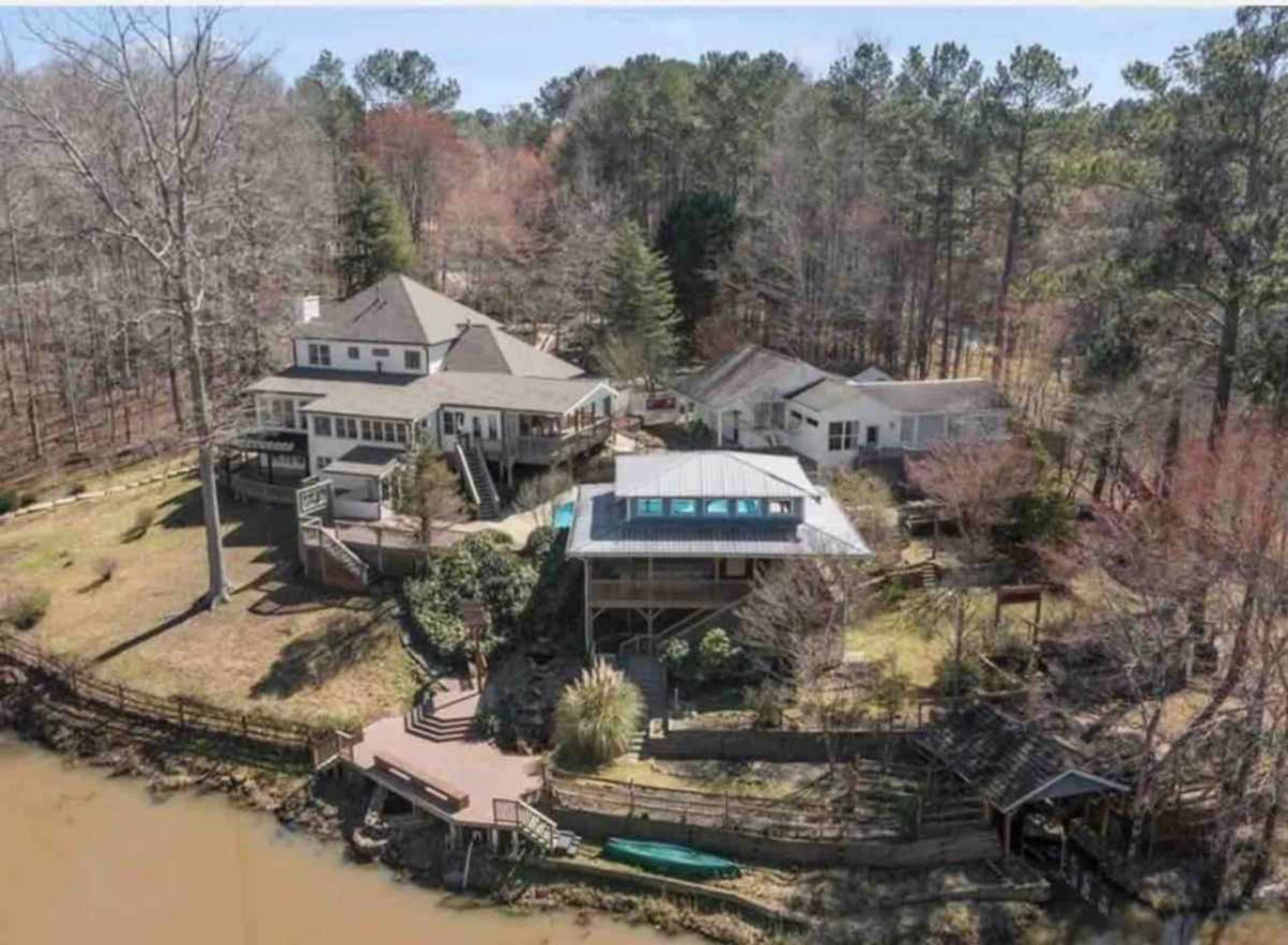 Aerial view of a multi-structure property near a body of water, surrounded by trees.