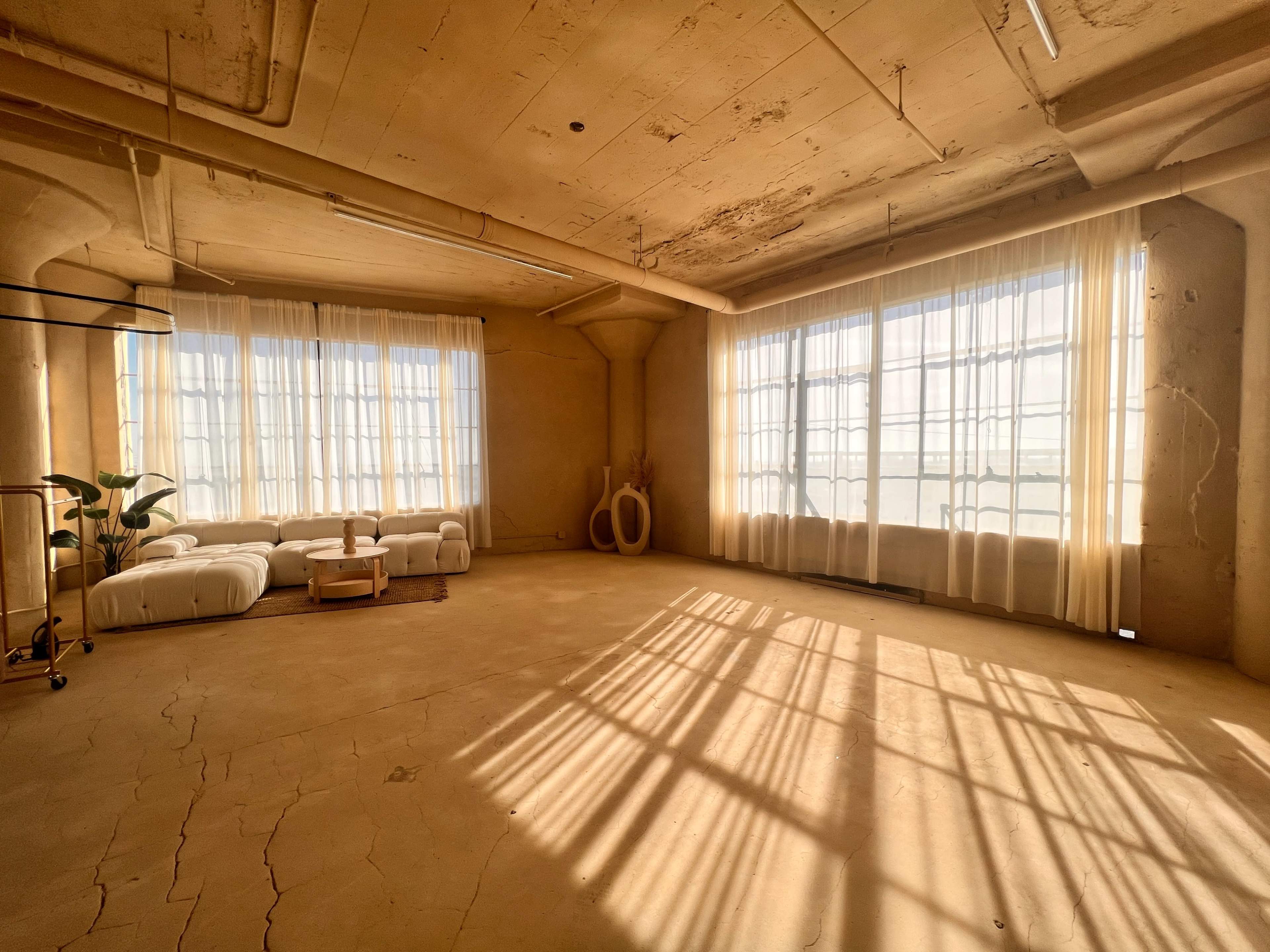 A spacious, empty room with large windows letting in natural light, highlighting the minimalist decor and concrete walls.