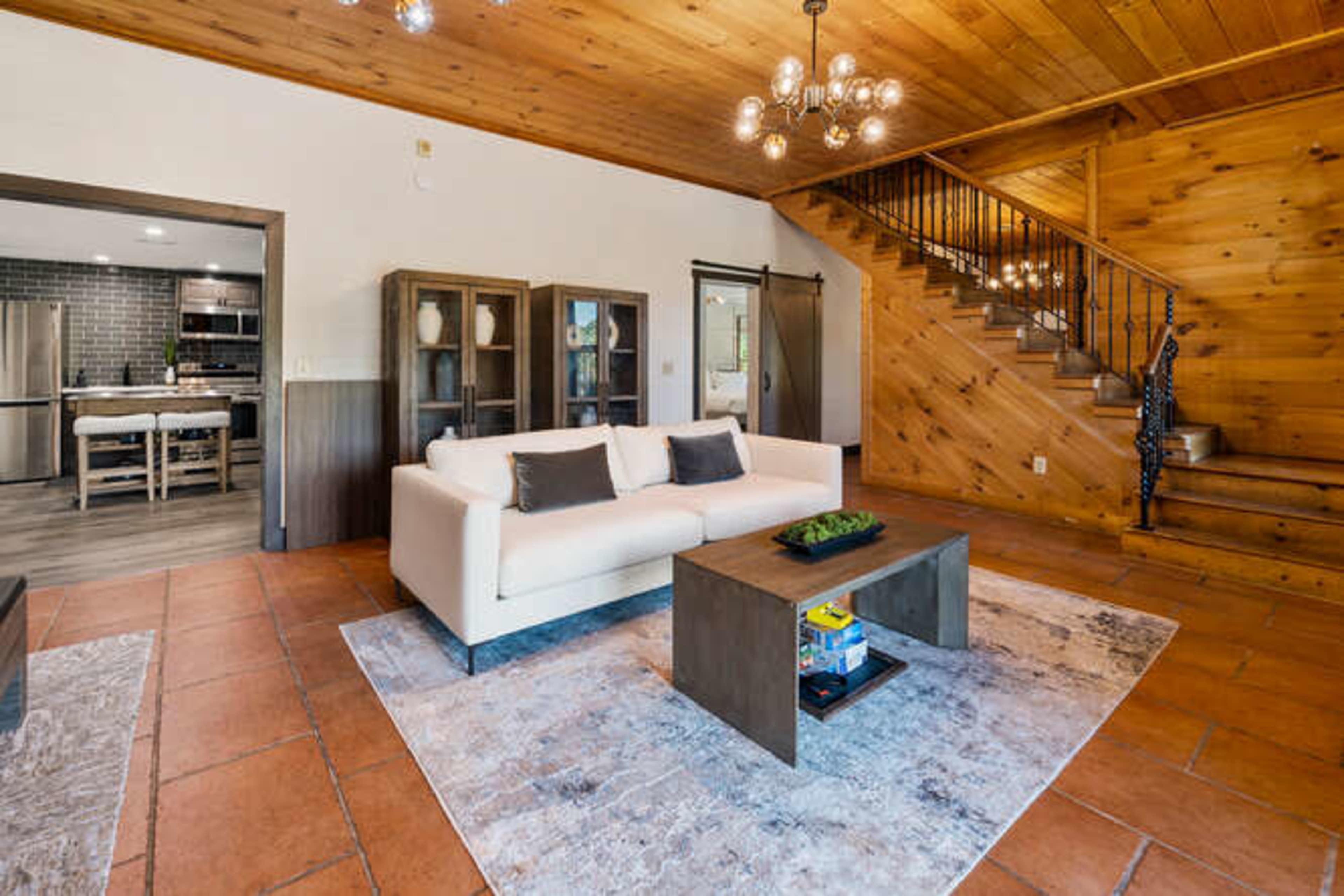 A living room area with a white sofa, a coffee table, and a staircase leading to an upper level, all set in a wooden interior.