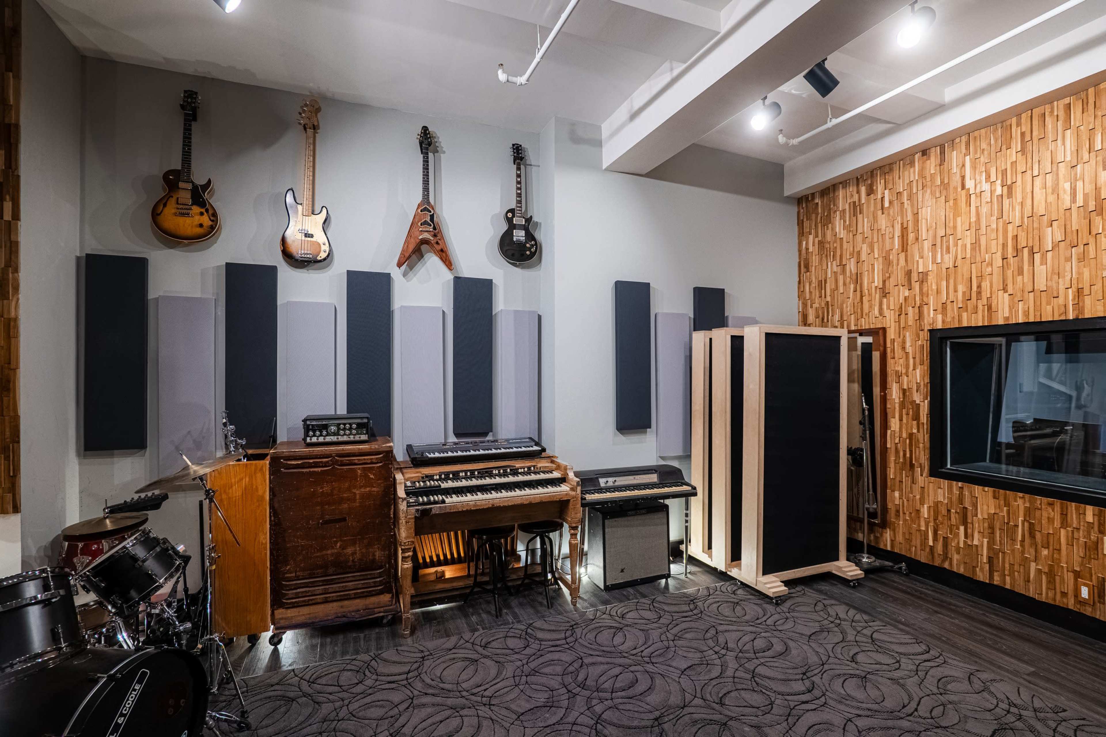 The image shows a sound studio featuring guitars mounted on the wall, various musical instruments, and acoustic panels arranged for optimal sound quality.