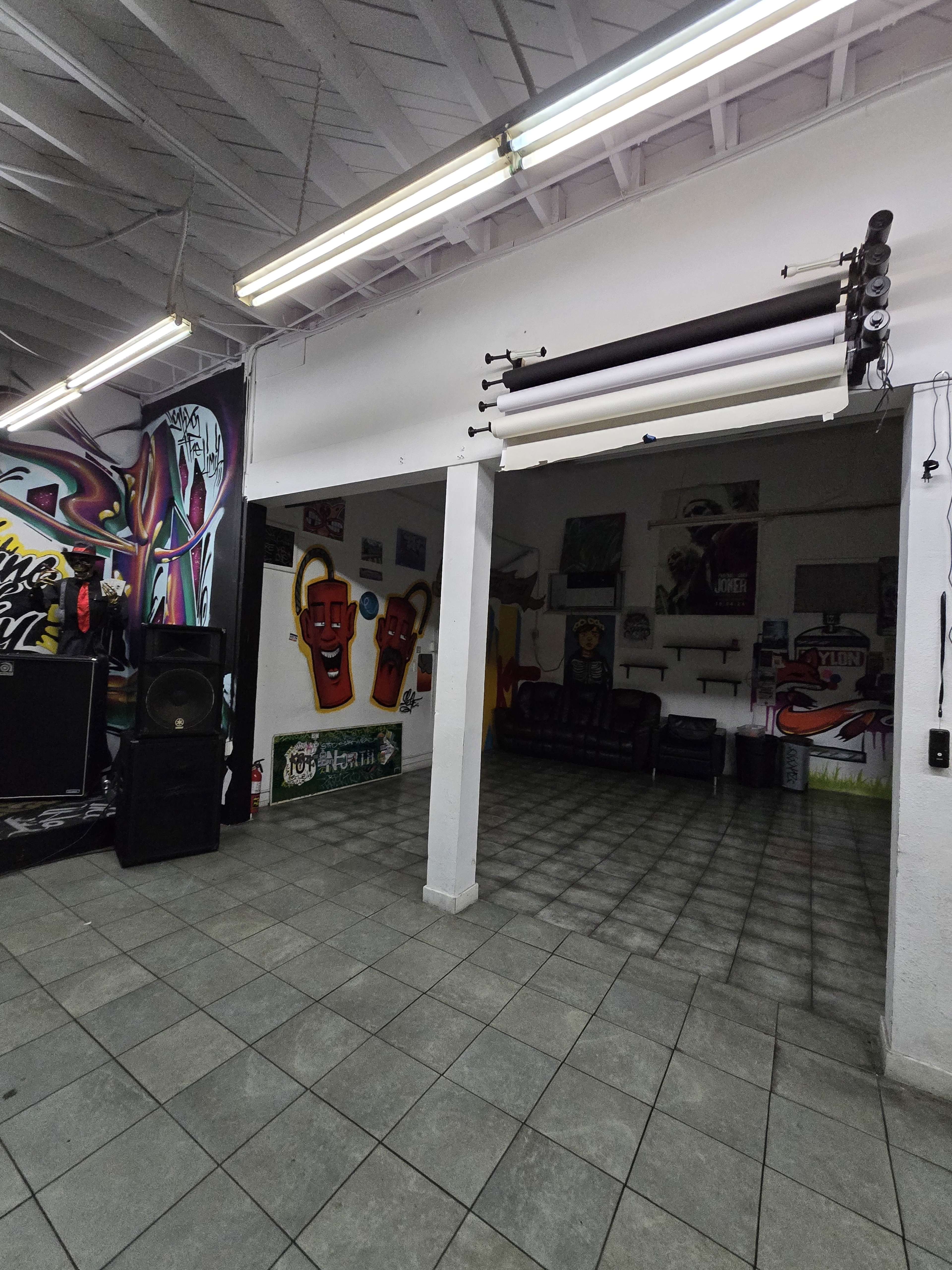 The image shows an indoor space featuring graffiti art on the walls, a tiled floor, and a few furniture pieces, including speakers and couches.