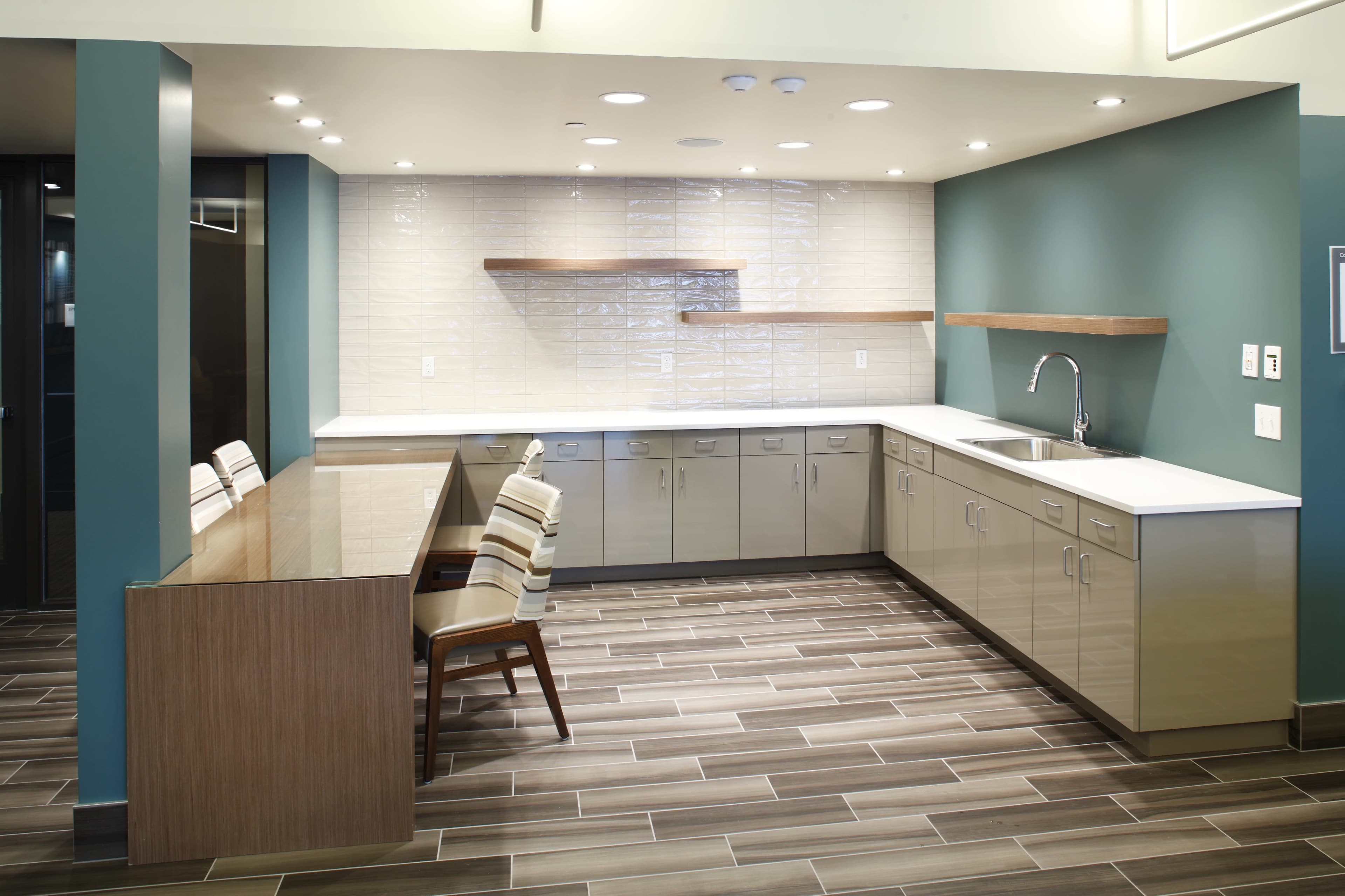 The image shows a modern kitchen with glossy cabinets, a countertop, and a wooden table accompanied by striped chairs.
