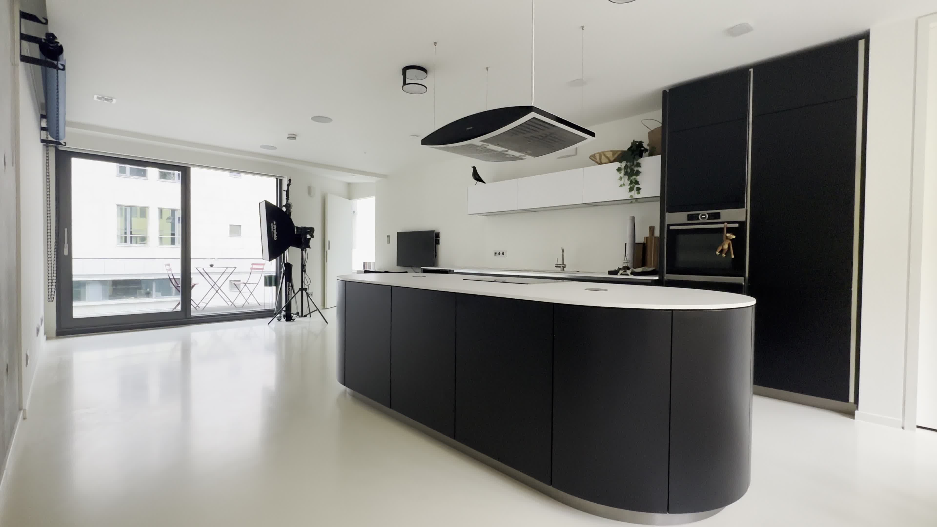 A modern kitchen featuring a large black island, sleek cabinetry, and large windows leading to a balcony.