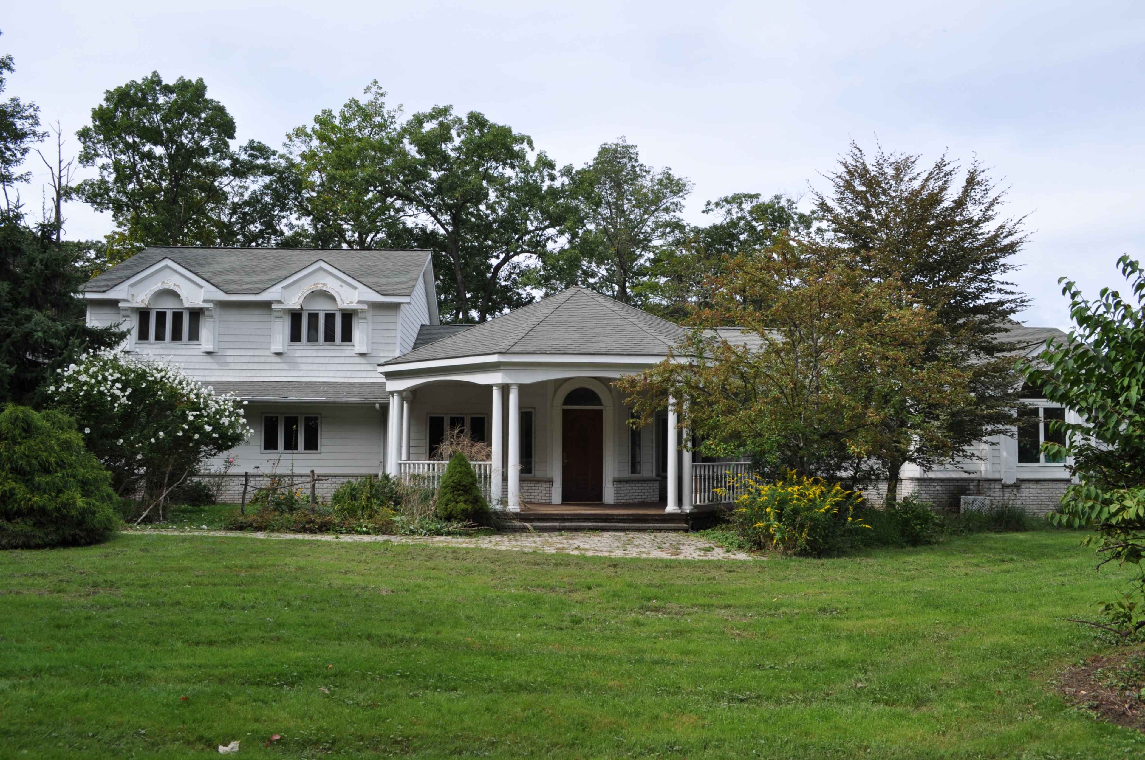 A two-story white house with a covered porch and surrounded by greenery.