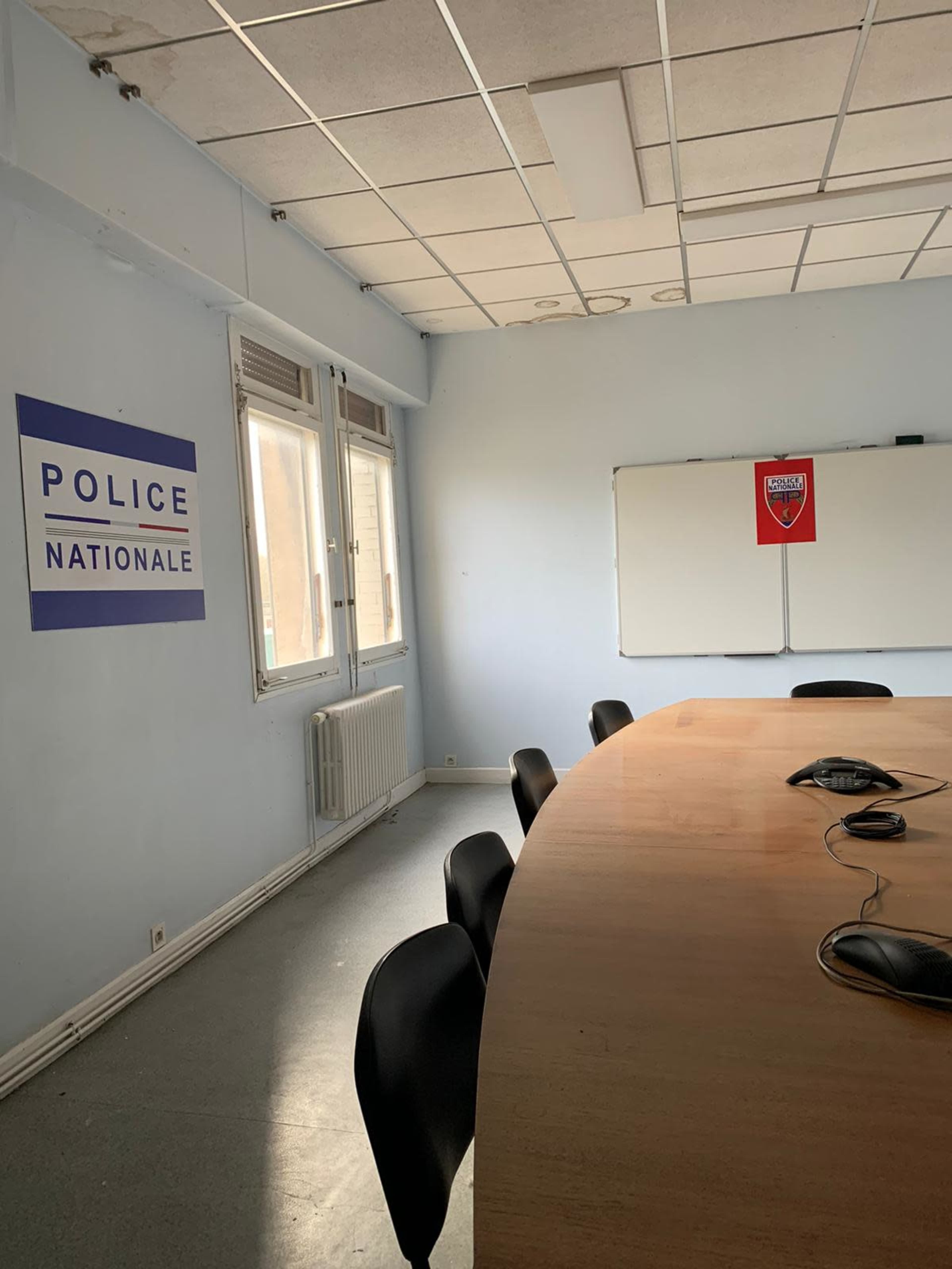 A meeting room with a large wooden table, several black chairs, and walls adorned with signs for "Police Nationale" and a sports team emblem, along with a whiteboard.