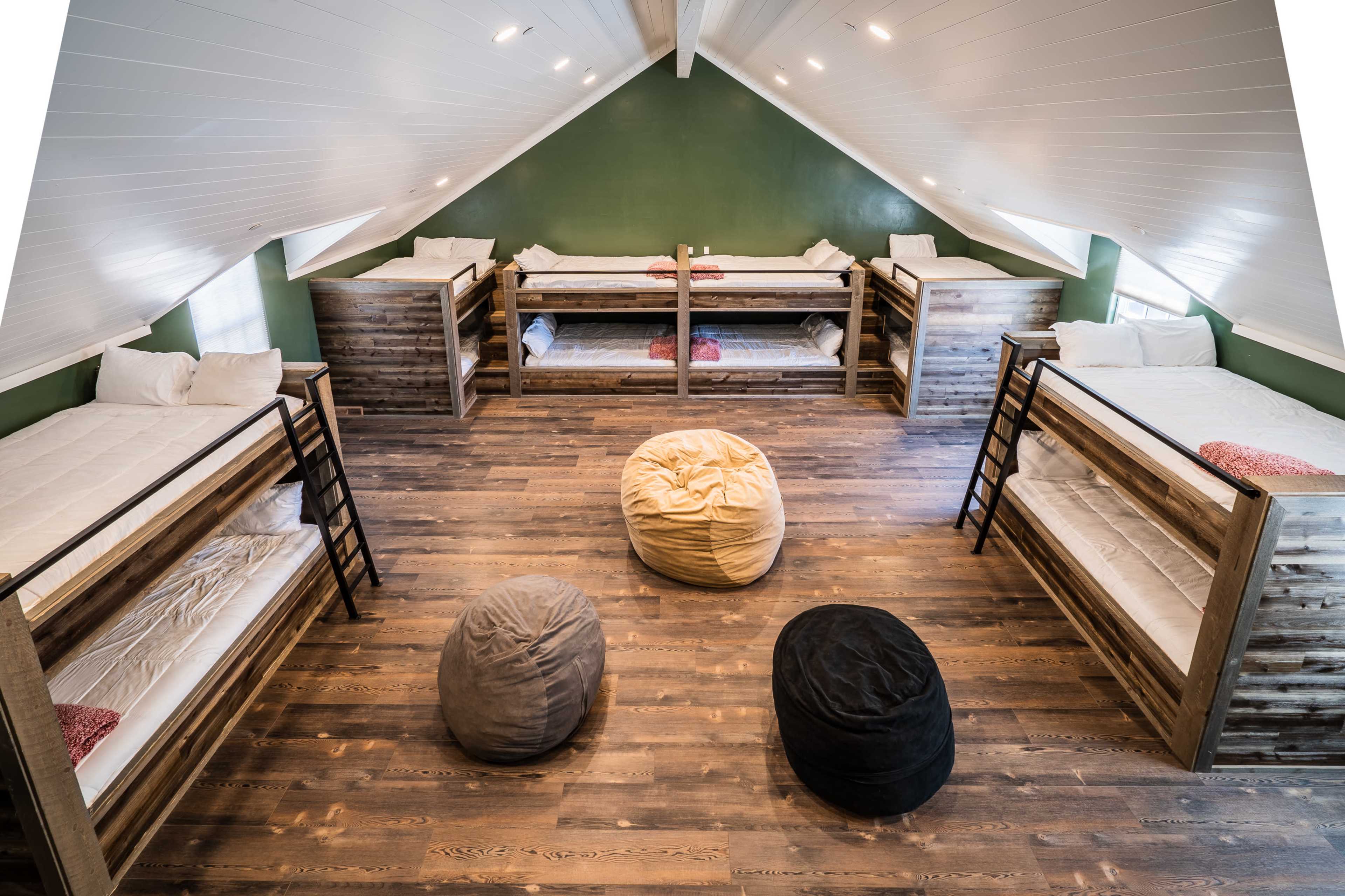 A spacious attic room featuring four sets of wooden bunk beds arranged around a wooden floor, with several bean bags positioned in the center.