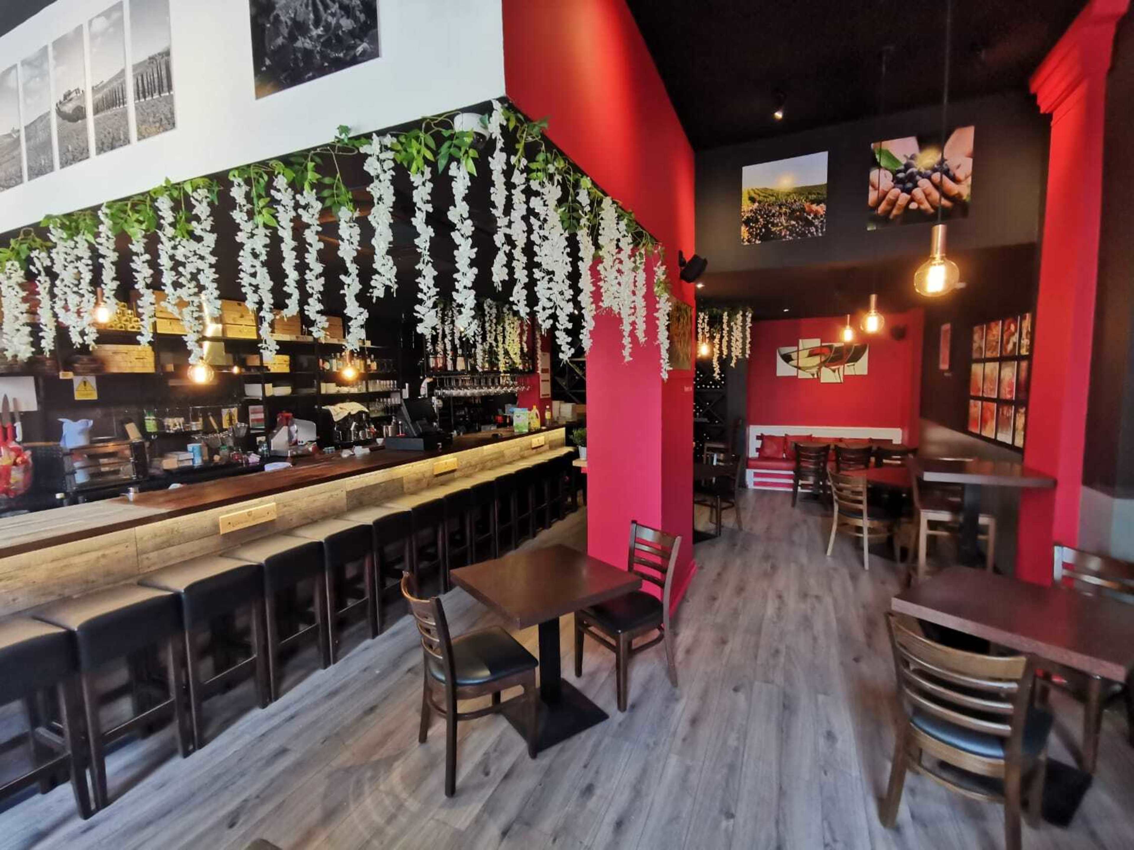 A modern café interior featuring a bar with seating, wooden tables, and decorative hanging plants.