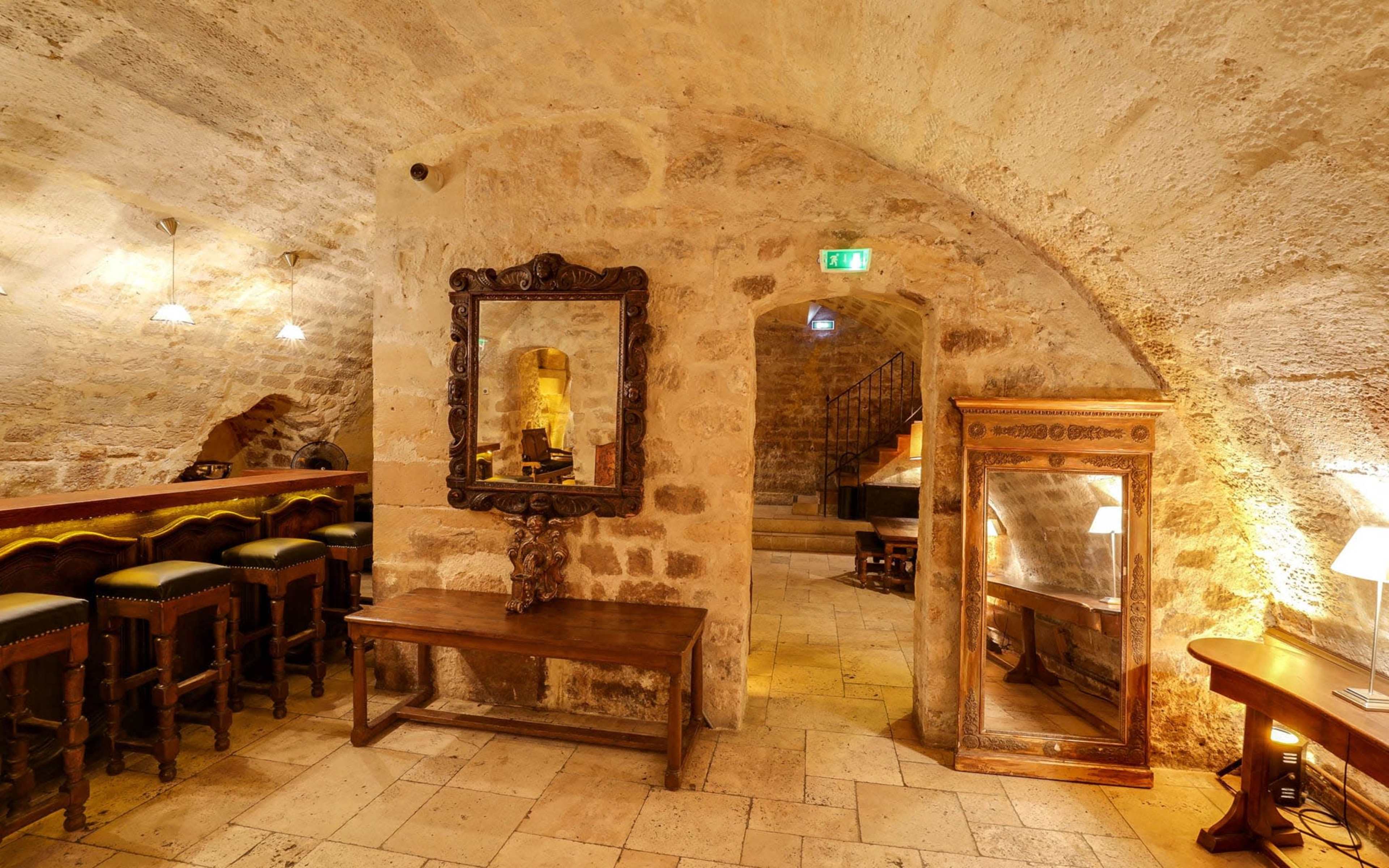 A rustic stone interior with arches, featuring wooden furniture, mirrors, and illuminated by warm lighting.
