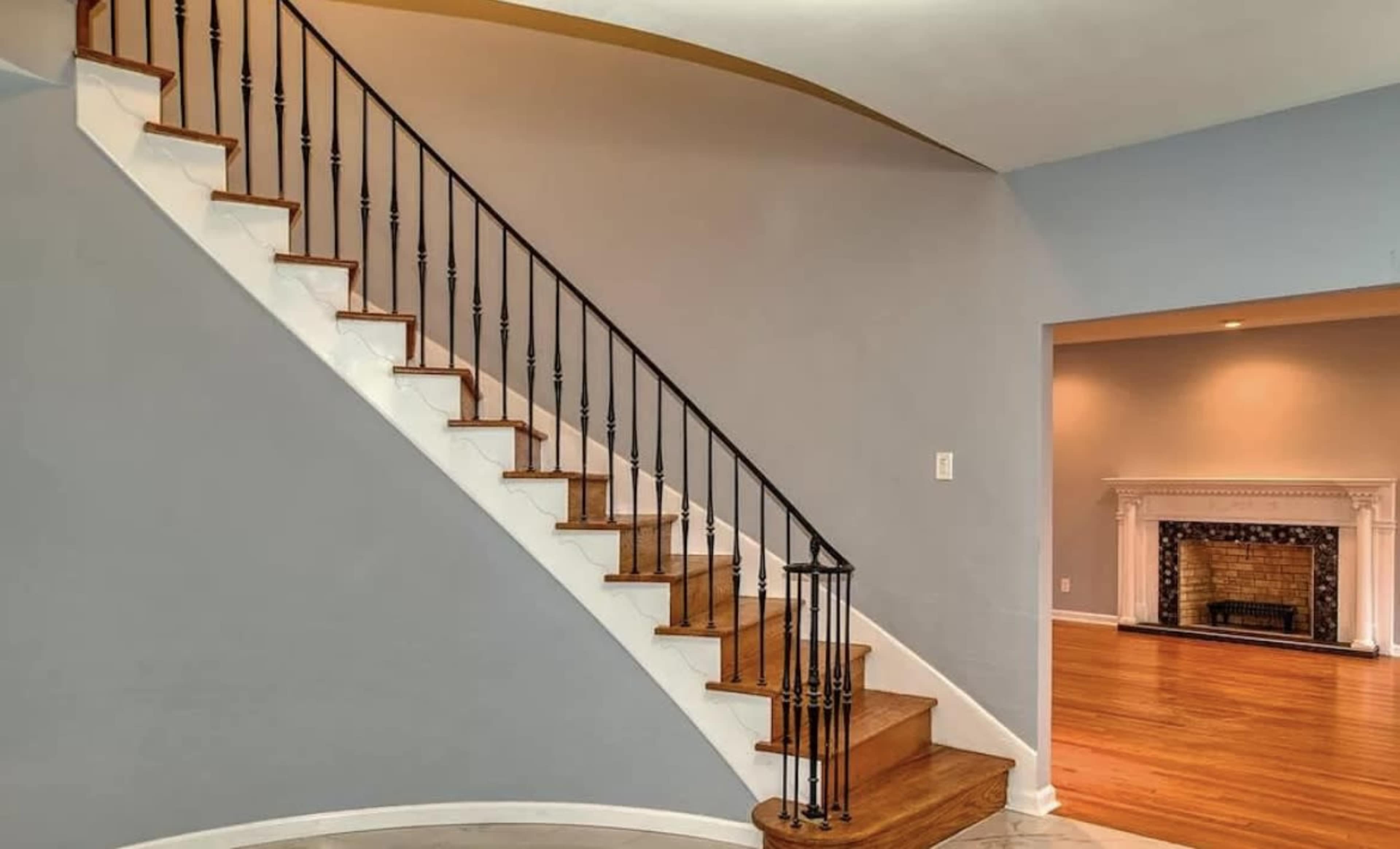 The image shows a curved staircase with wooden steps and black railings, leading to a hallway with a fireplace at the far end.