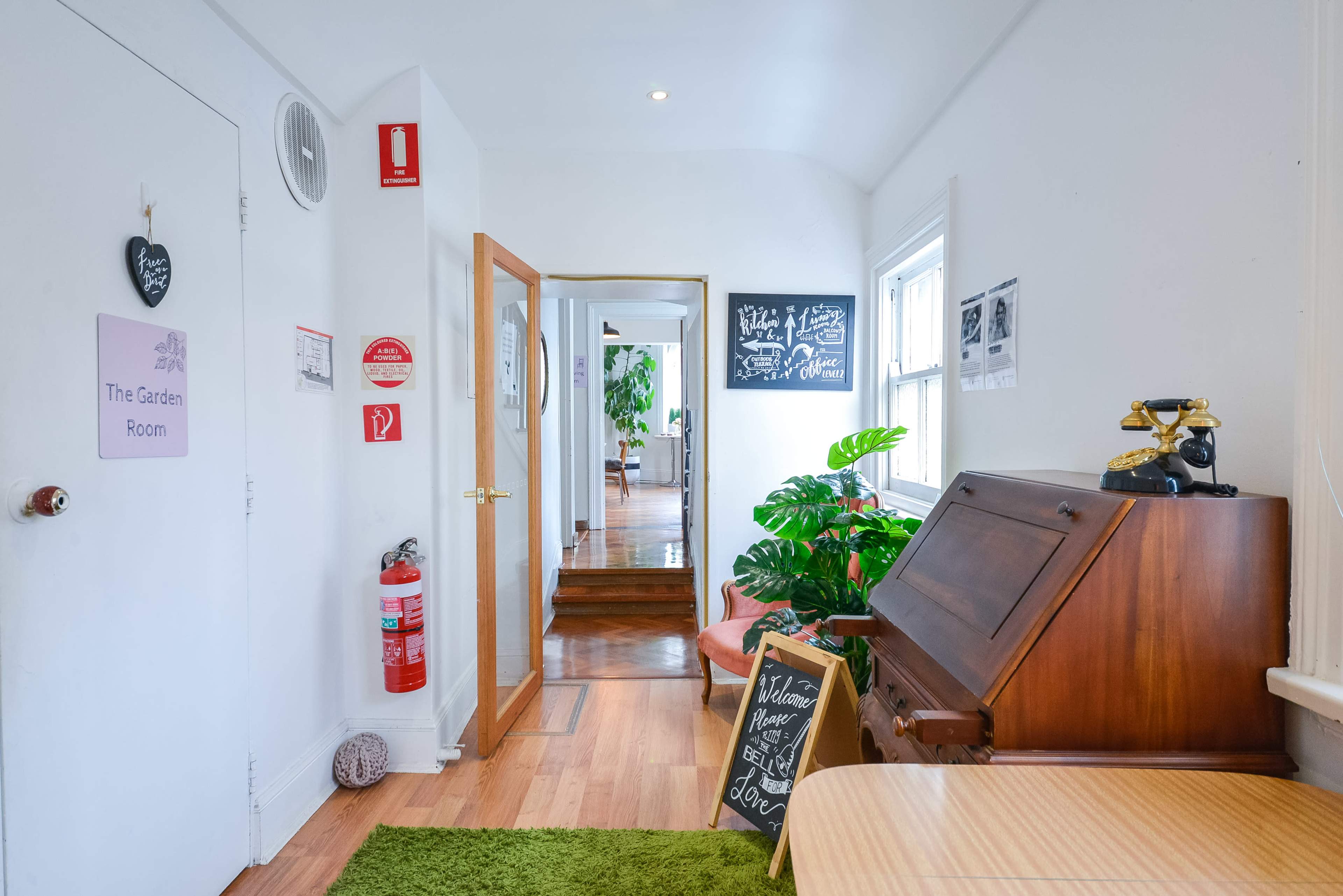 A hallway featuring a wooden desk, potted plants, and various informational signs is seen leading to another room.