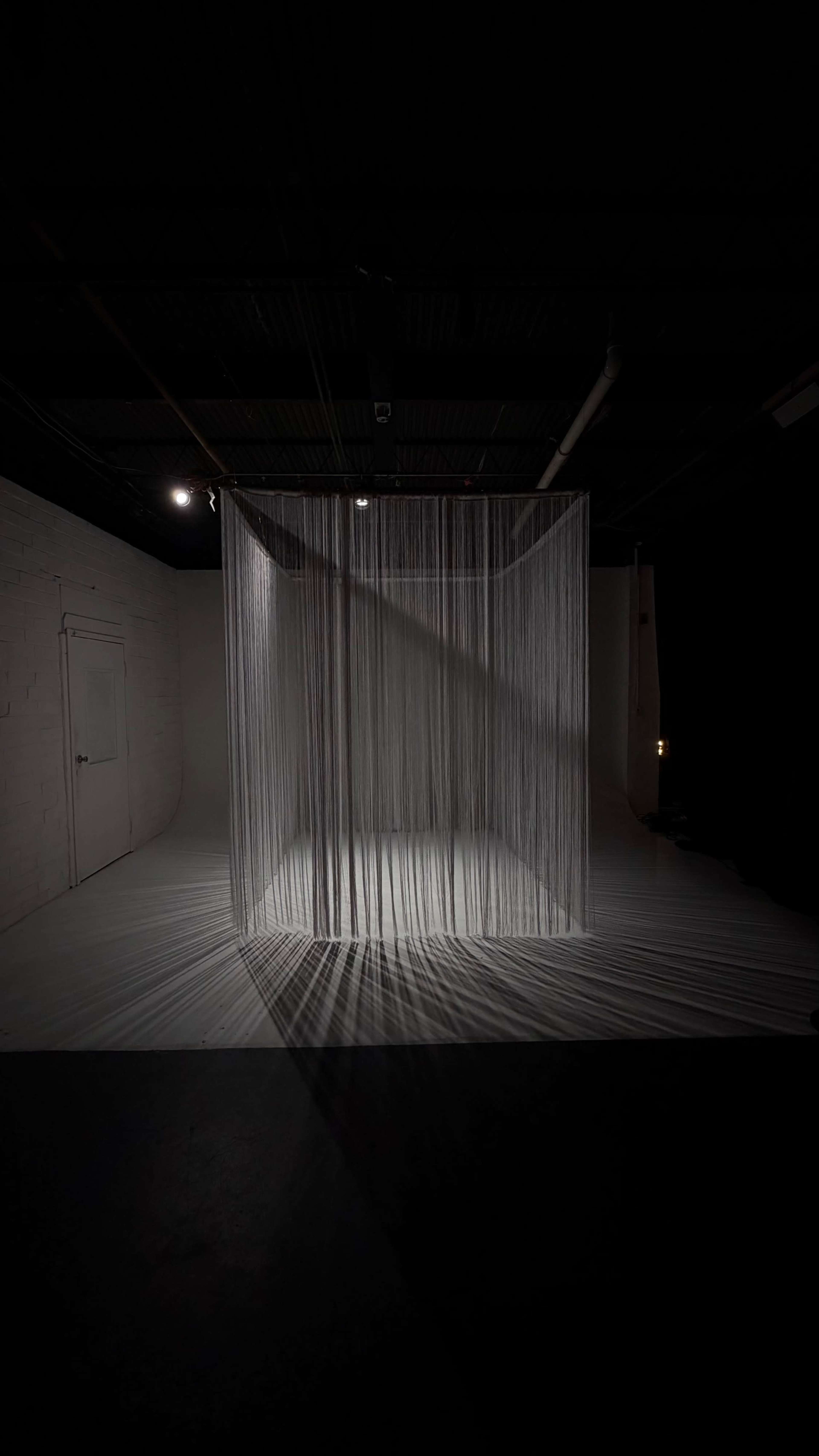 A space featuring a translucent curtain made of vertical threads, casting shadows on the floor in a dimly lit environment.