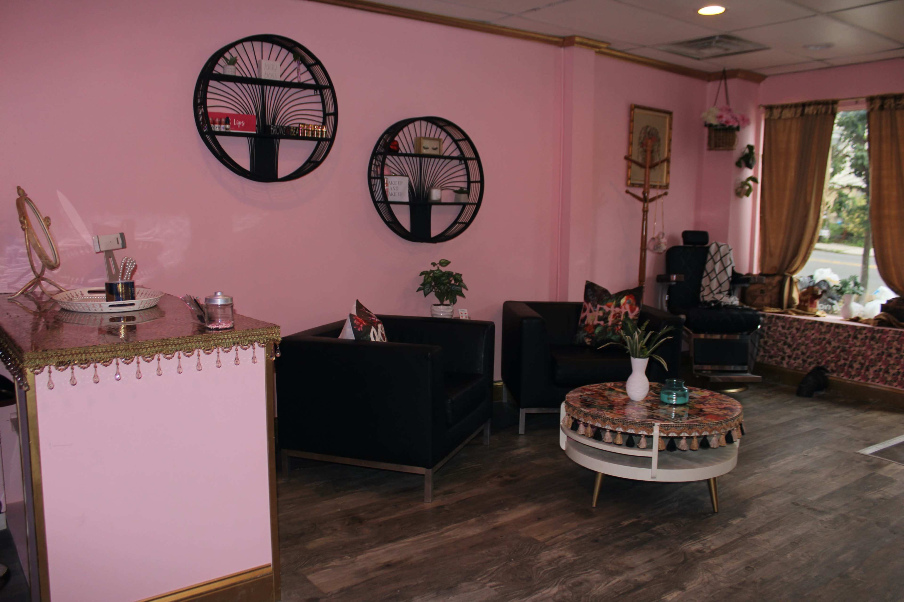 The interior of a pink-themed salon with black seating, decorative wall art, and a small table in the center.