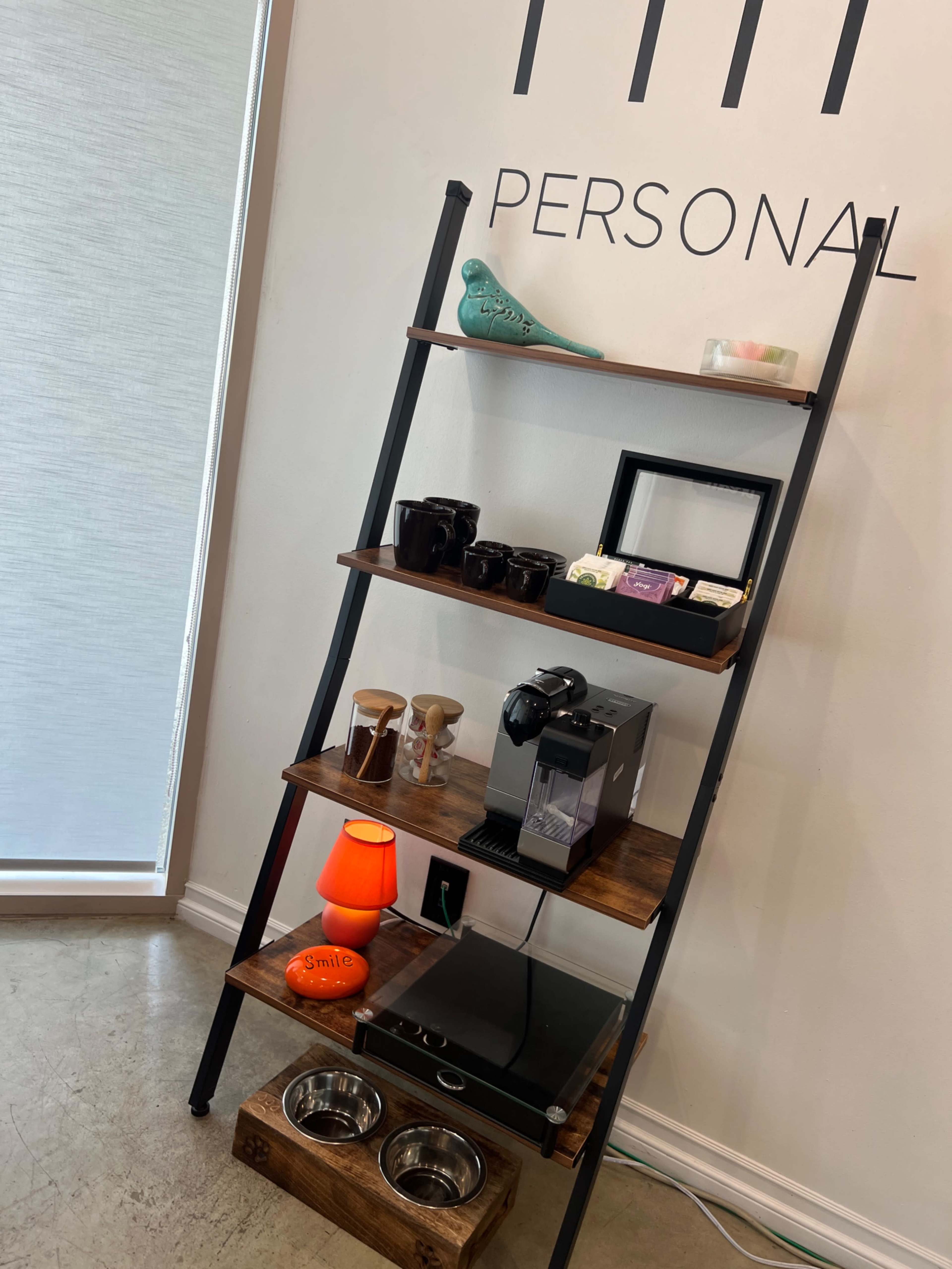 The image shows a wooden ladder shelf featuring a coffee machine, mugs, a picture frame, and decorative items, along with a pet food bowl at the bottom.