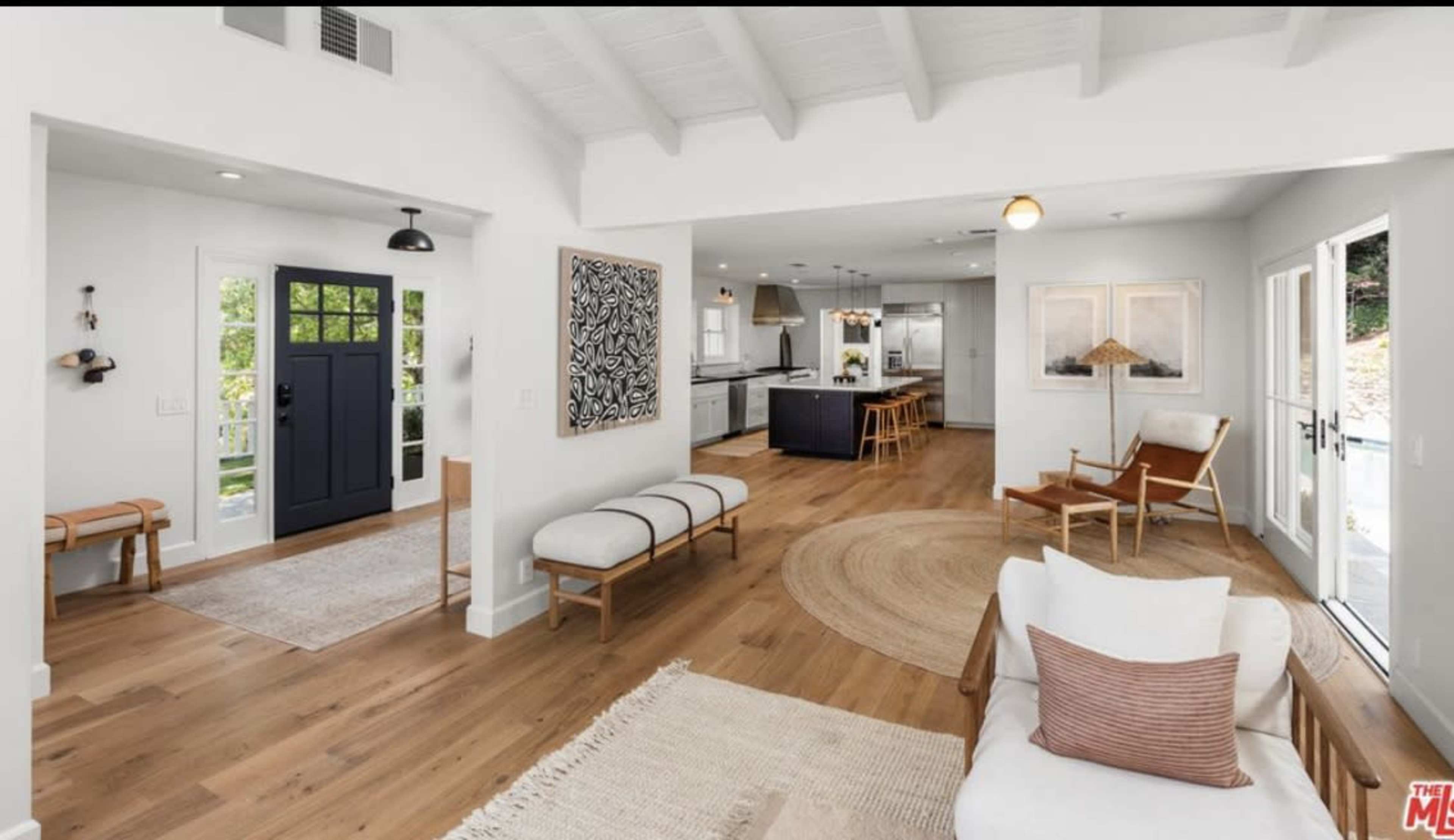 A bright, open-concept living space features a seating area, a hallway with a dark front door, and a view into a modern kitchen.