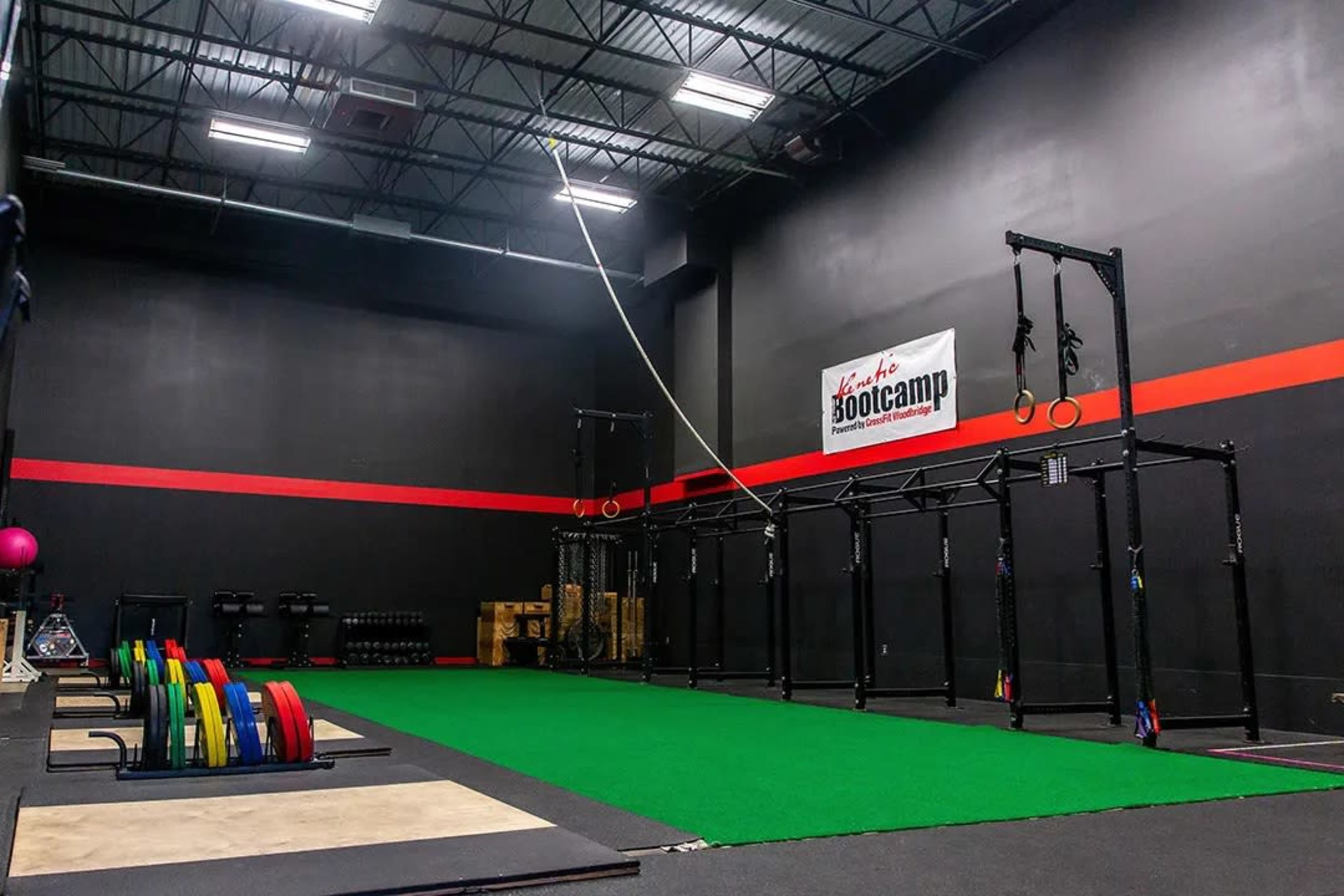 An indoor gym space equipped with weightlifting equipment, a green turf area, and a functional training rig with suspension straps.