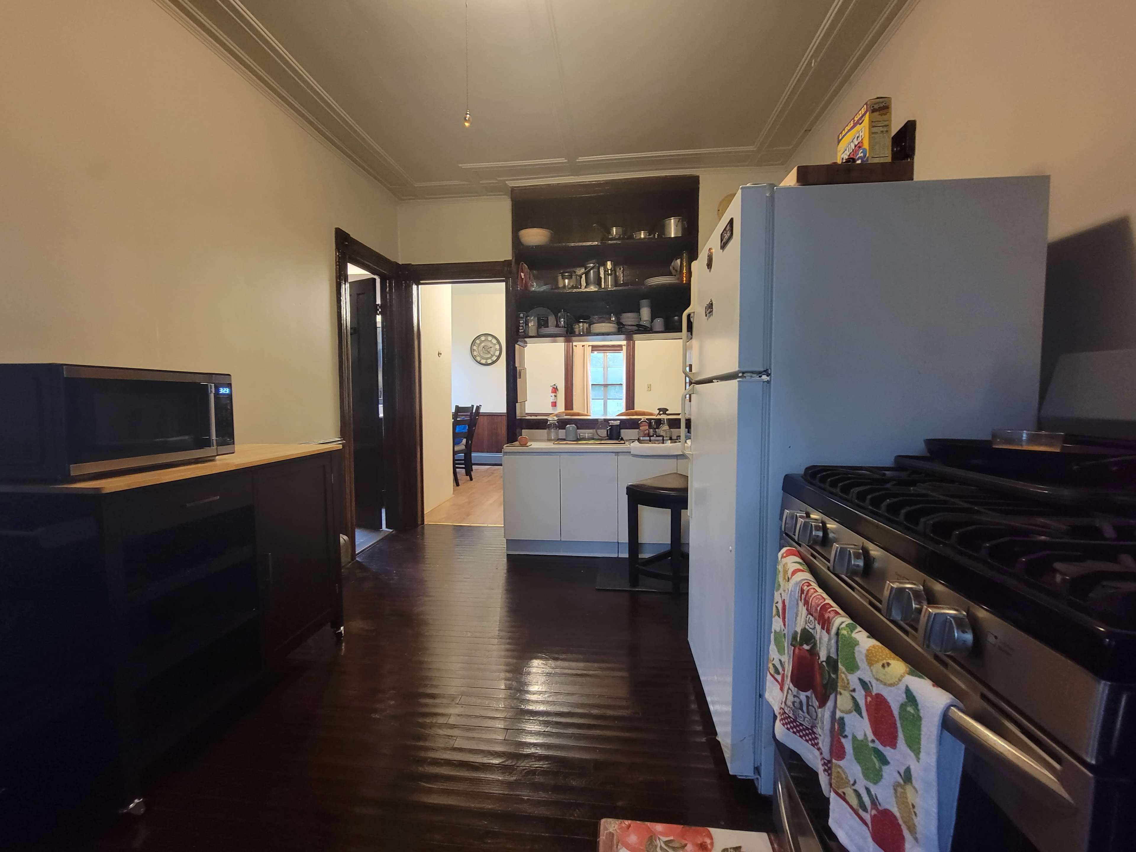 The image shows a kitchen with a black countertop, a microwave, a white refrigerator, and a stove, featuring an open layout that leads to a dining area in the background.