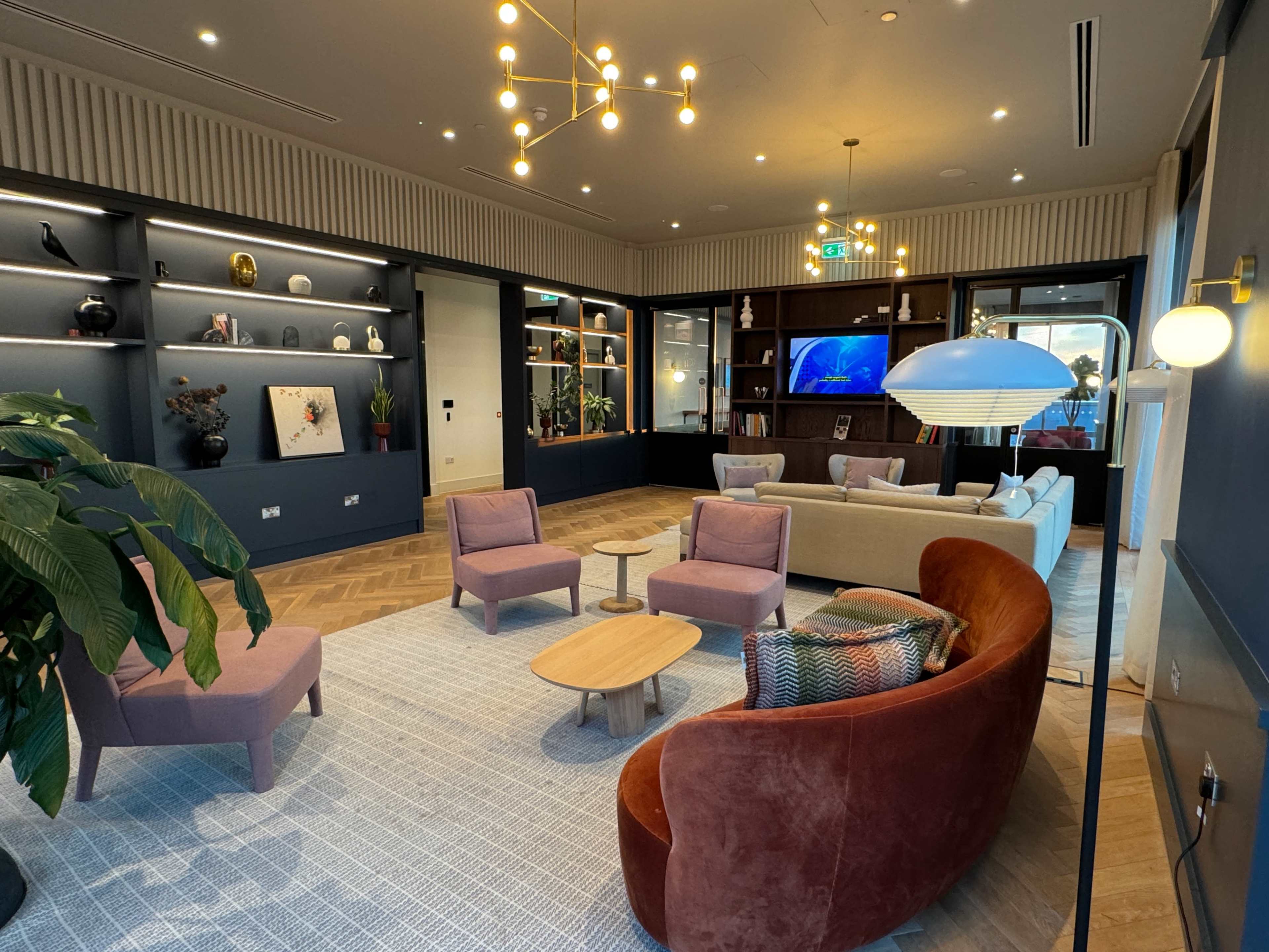 A modern lounge area with various seating arrangements, decorative shelves, and plants.