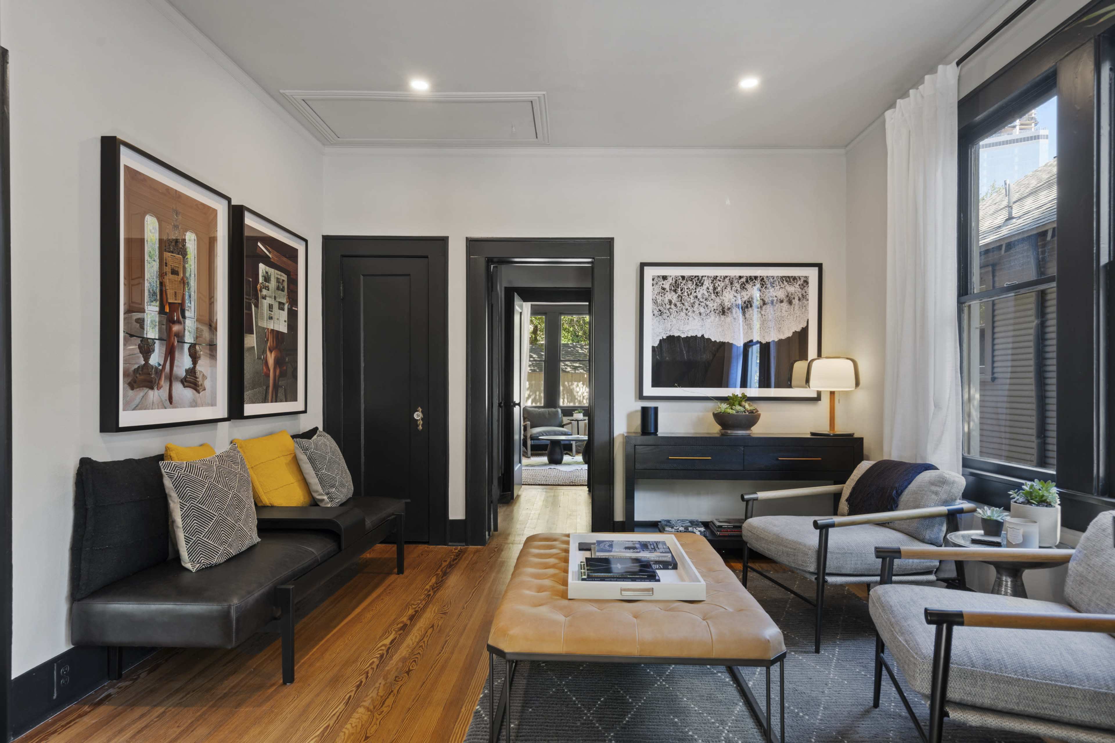 A modern living room with dark-framed artwork, a light-colored coffee table, and a mix of seating arrangements against a neutral wall.