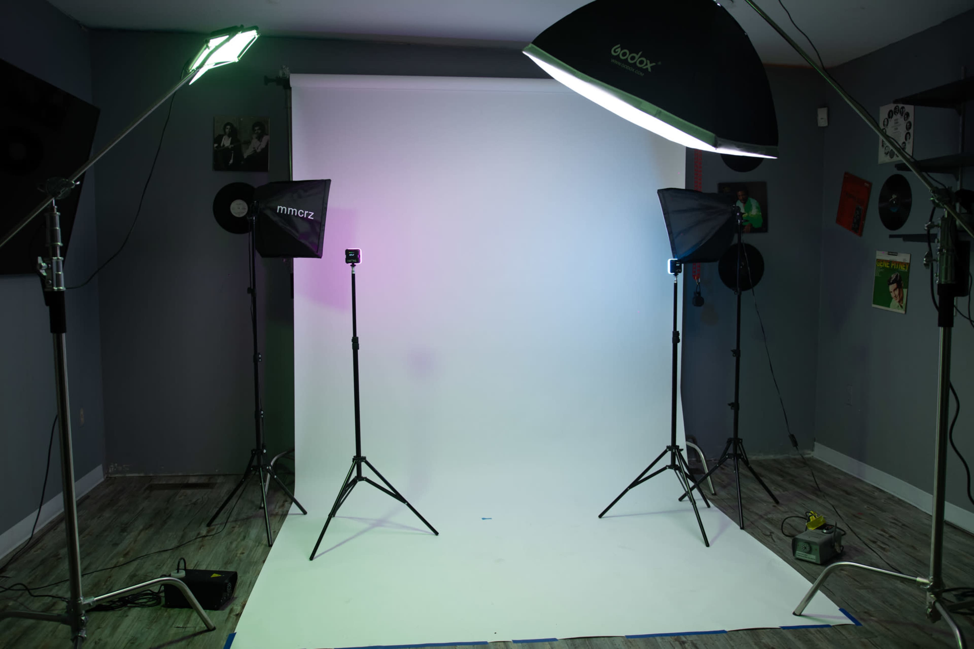 The image shows a photography studio setup with a seamless white backdrop, lighting equipment, and a wooden floor.