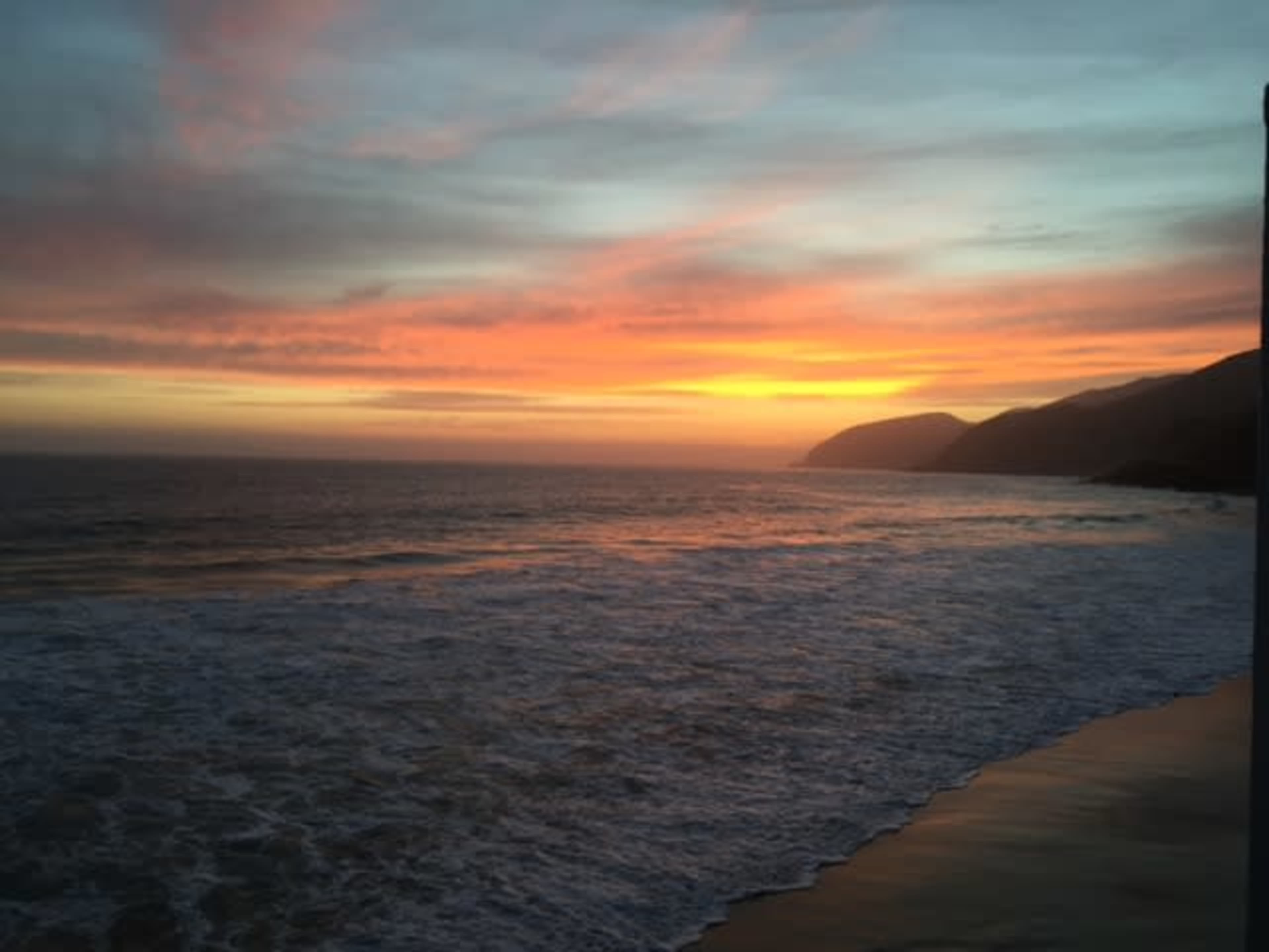 The image shows a coastline at sunset, with vibrant colors illuminating the sky over the ocean.
