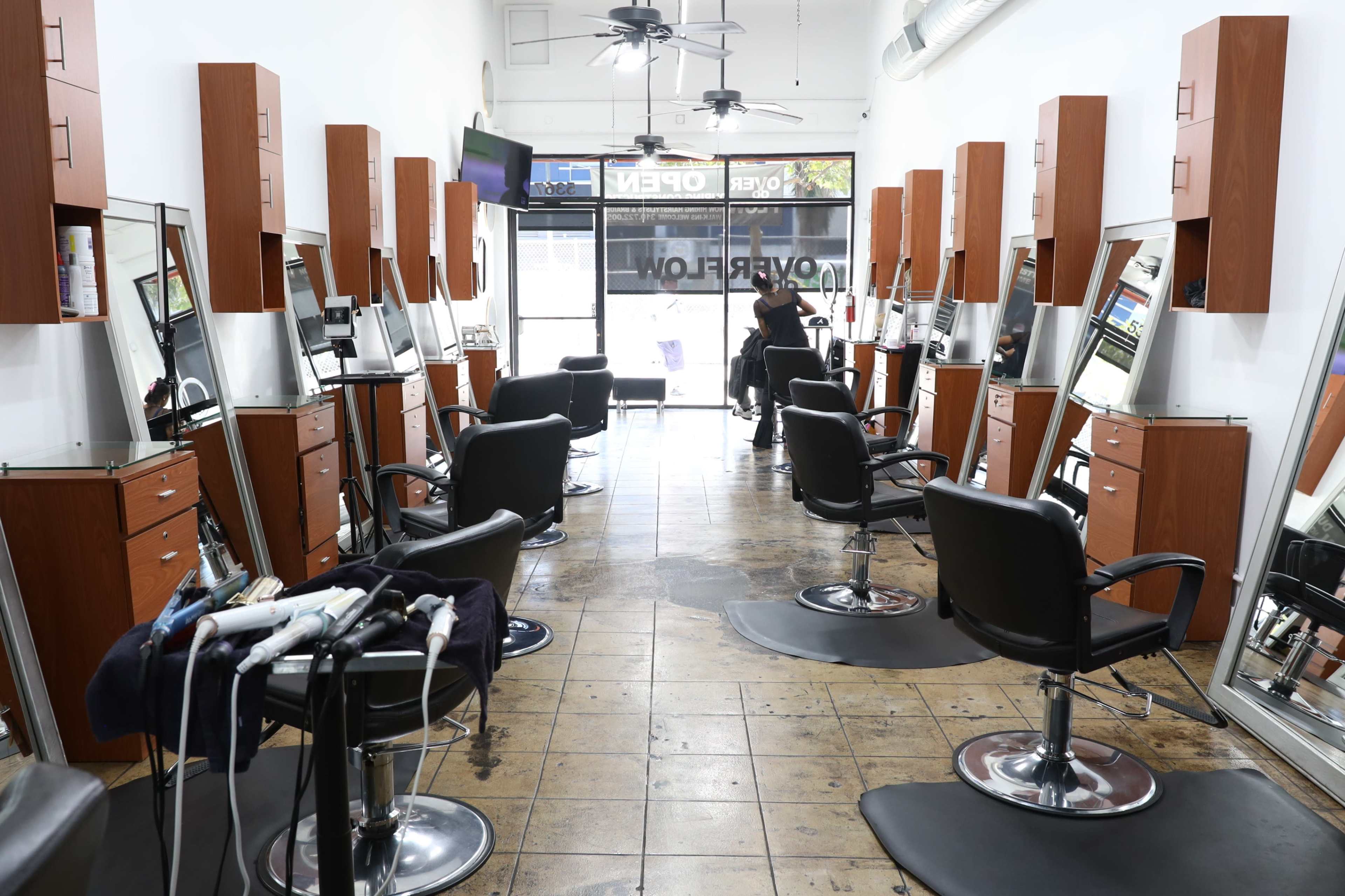 A hair salon with multiple styling stations featuring mirrors and chairs, and a stylist working in the background.