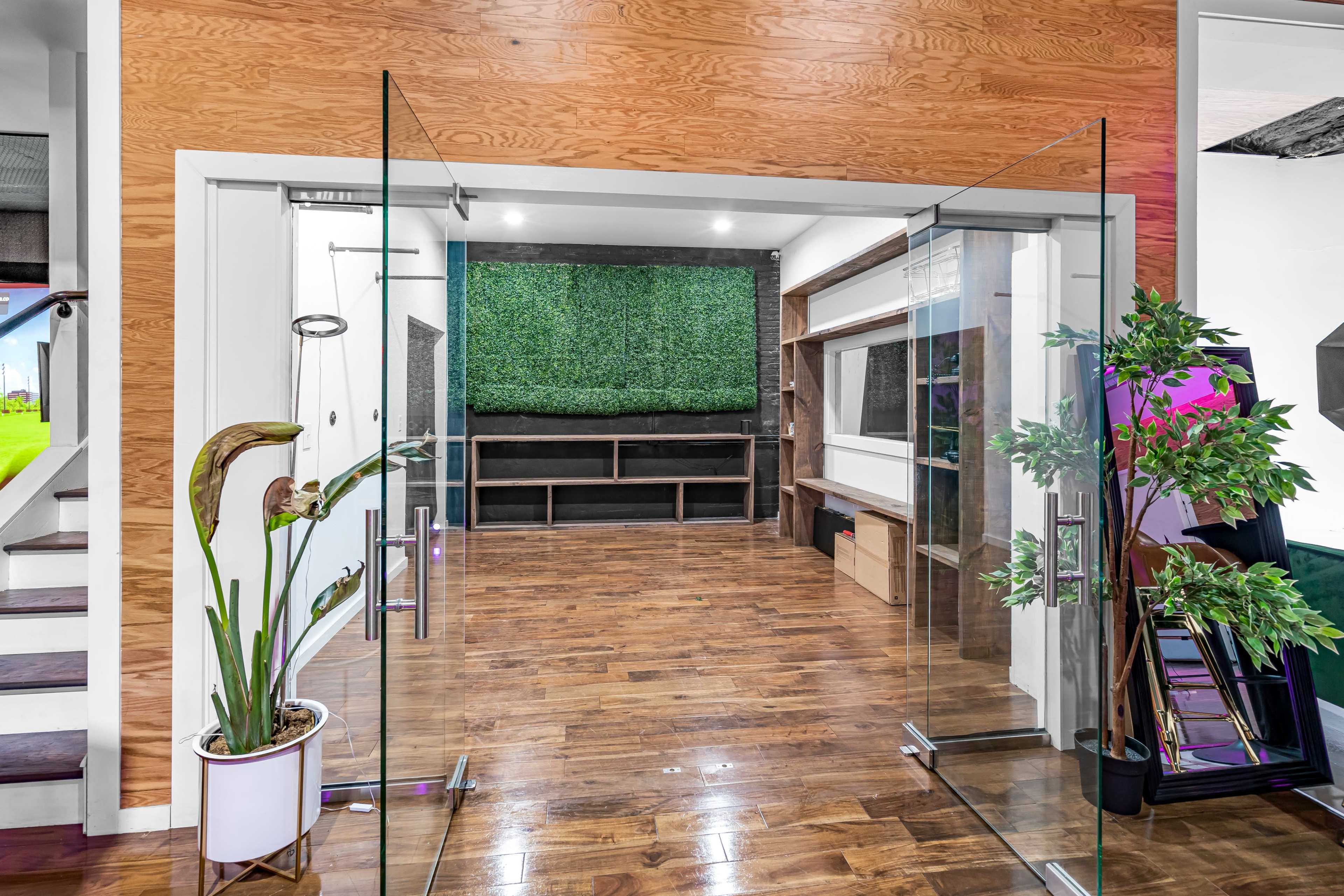 A modern interior space features glass double doors leading to a room with wood paneling, a green wall display, and built-in shelving.