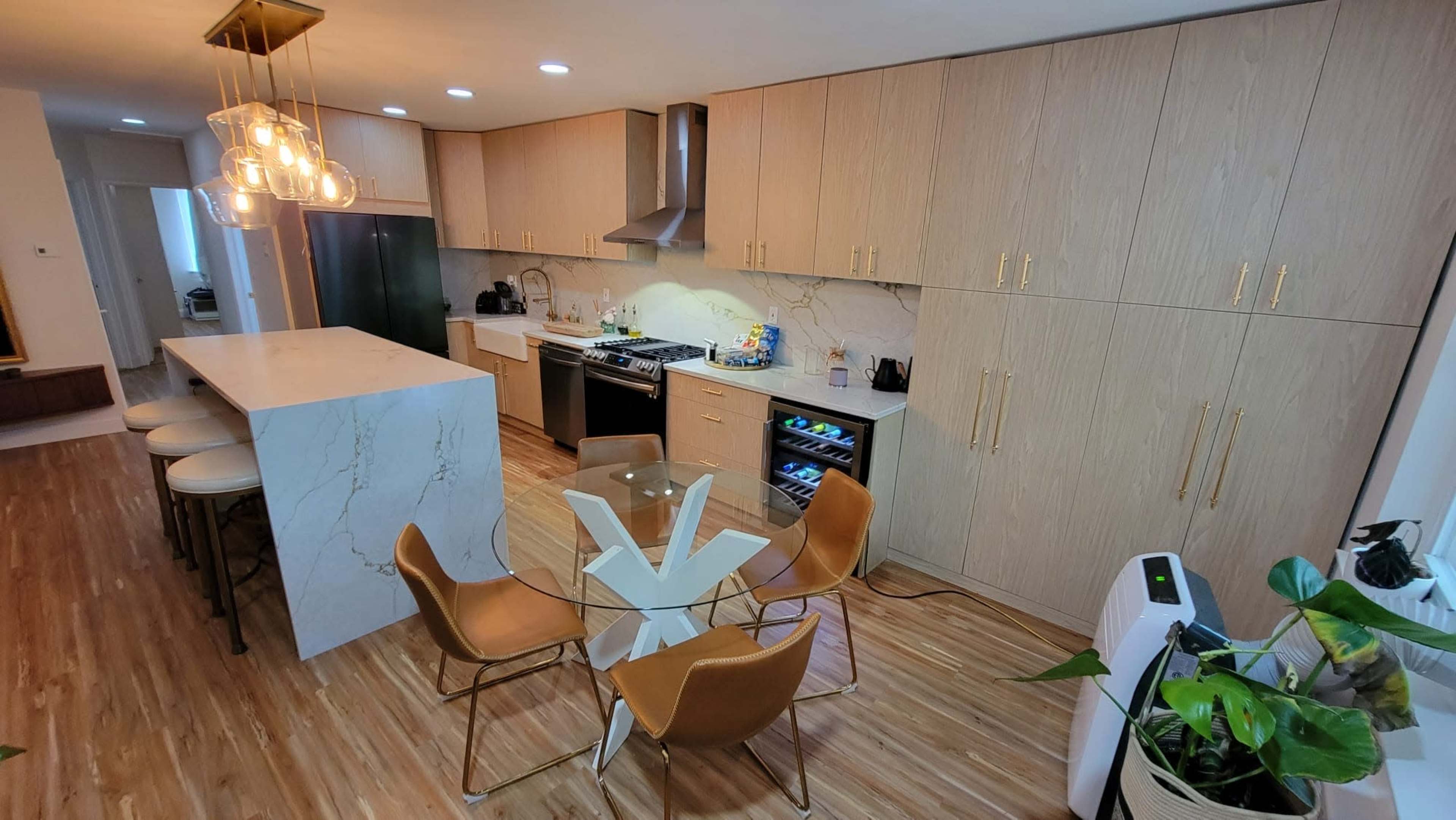 A modern kitchen features wooden cabinets, a marble island, stainless steel appliances, and a glass dining table surrounded by stylish chairs.