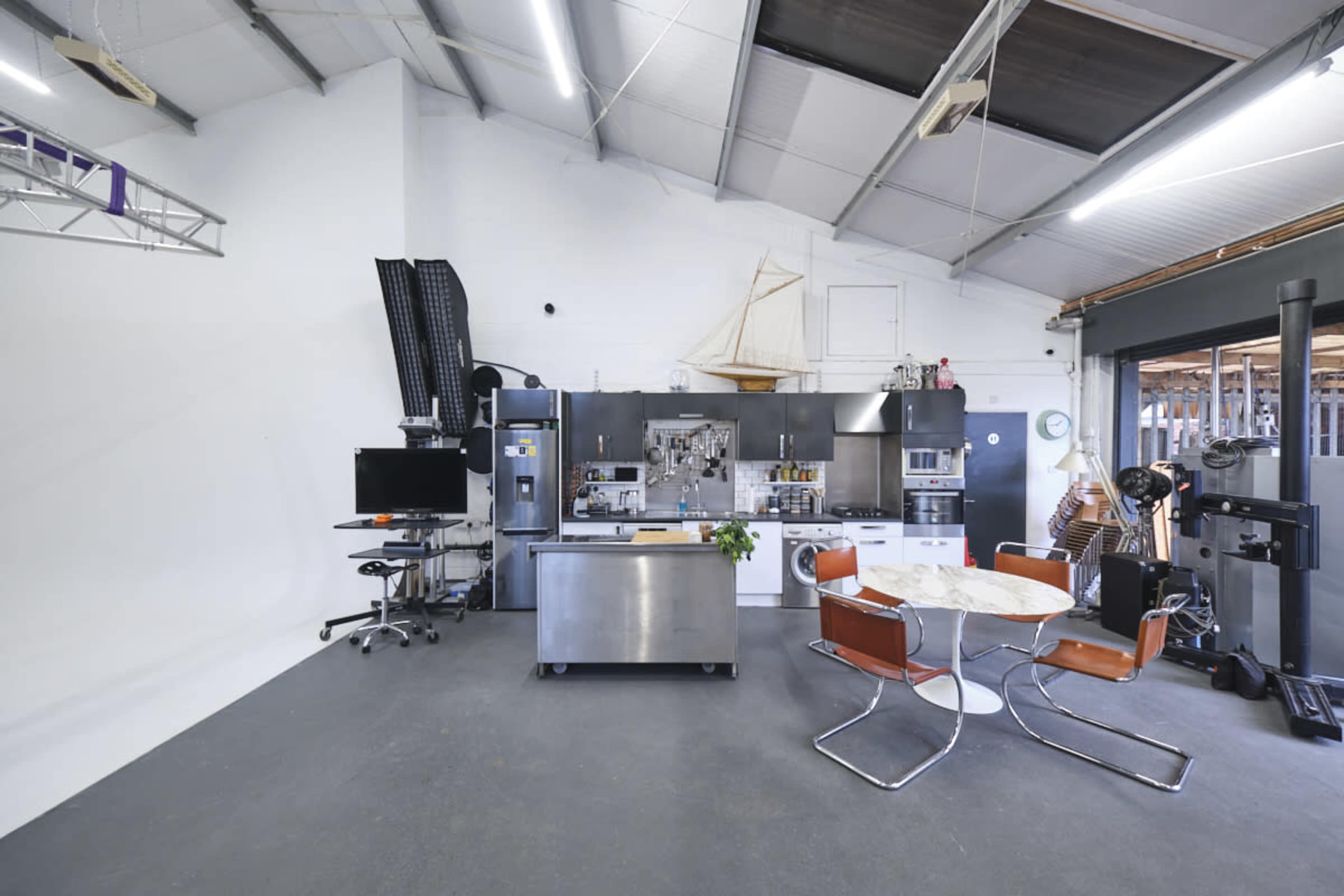 A spacious industrial kitchen area with a large steel island, modern appliances, a round dining table with four orange chairs, and a wall featuring shelves and nautical decor.