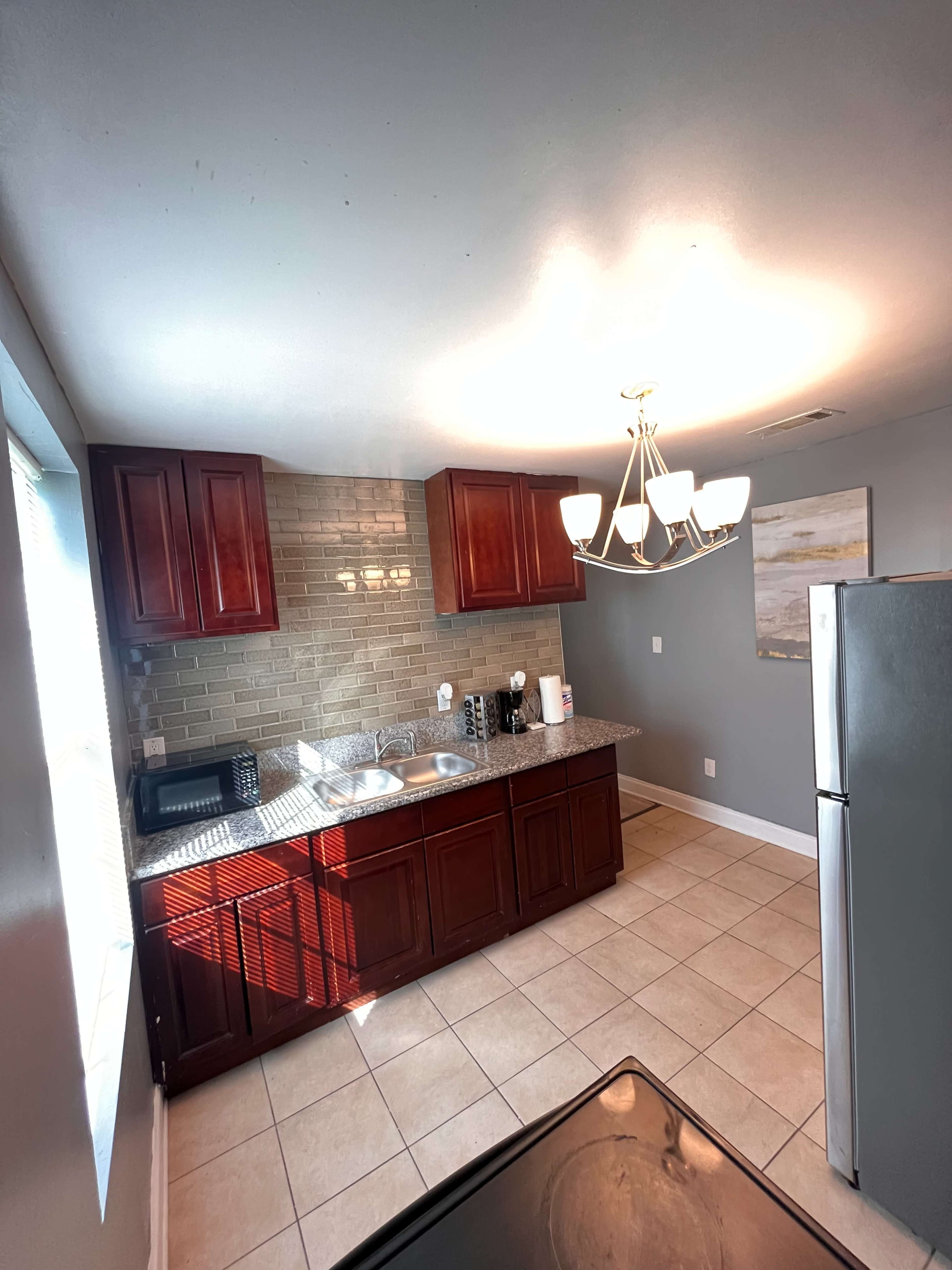 The image shows a kitchen with red cabinetry, a stainless steel refrigerator, and a sink beneath a decorative light fixture.