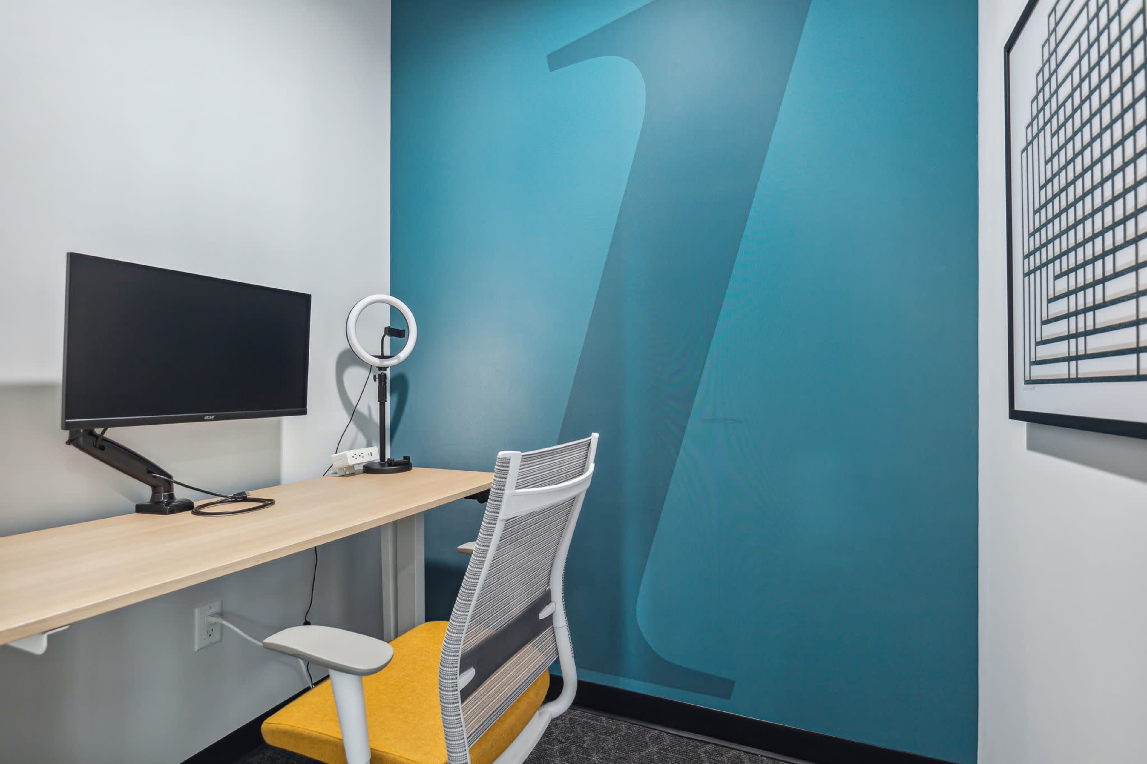 The image shows a small workspace featuring a monitor on a desk, a ring light, and a chair in front of a teal wall with a large "Z" graphic.