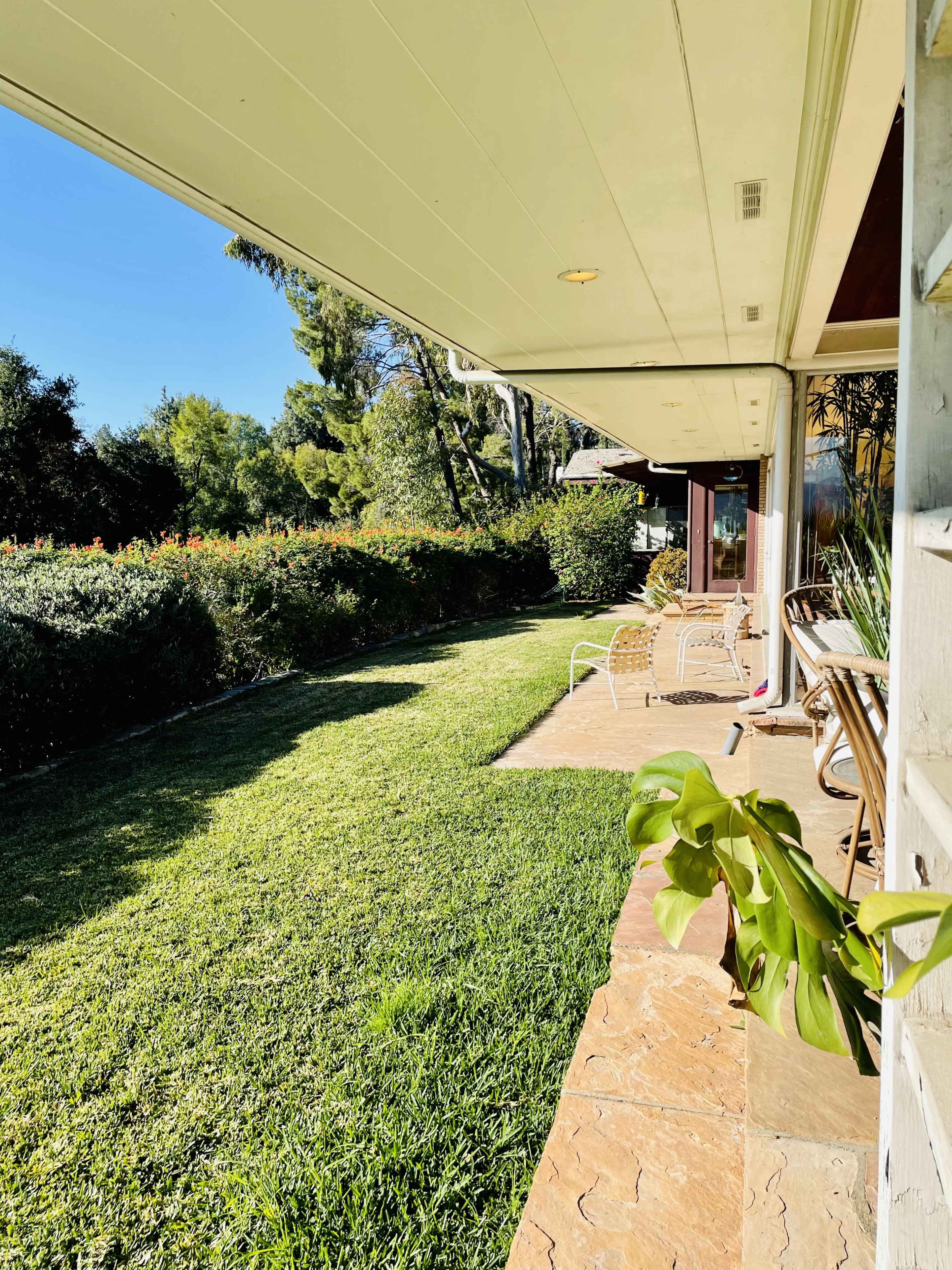 The image shows a grassy yard beside a house with a stone pathway and outdoor seating.