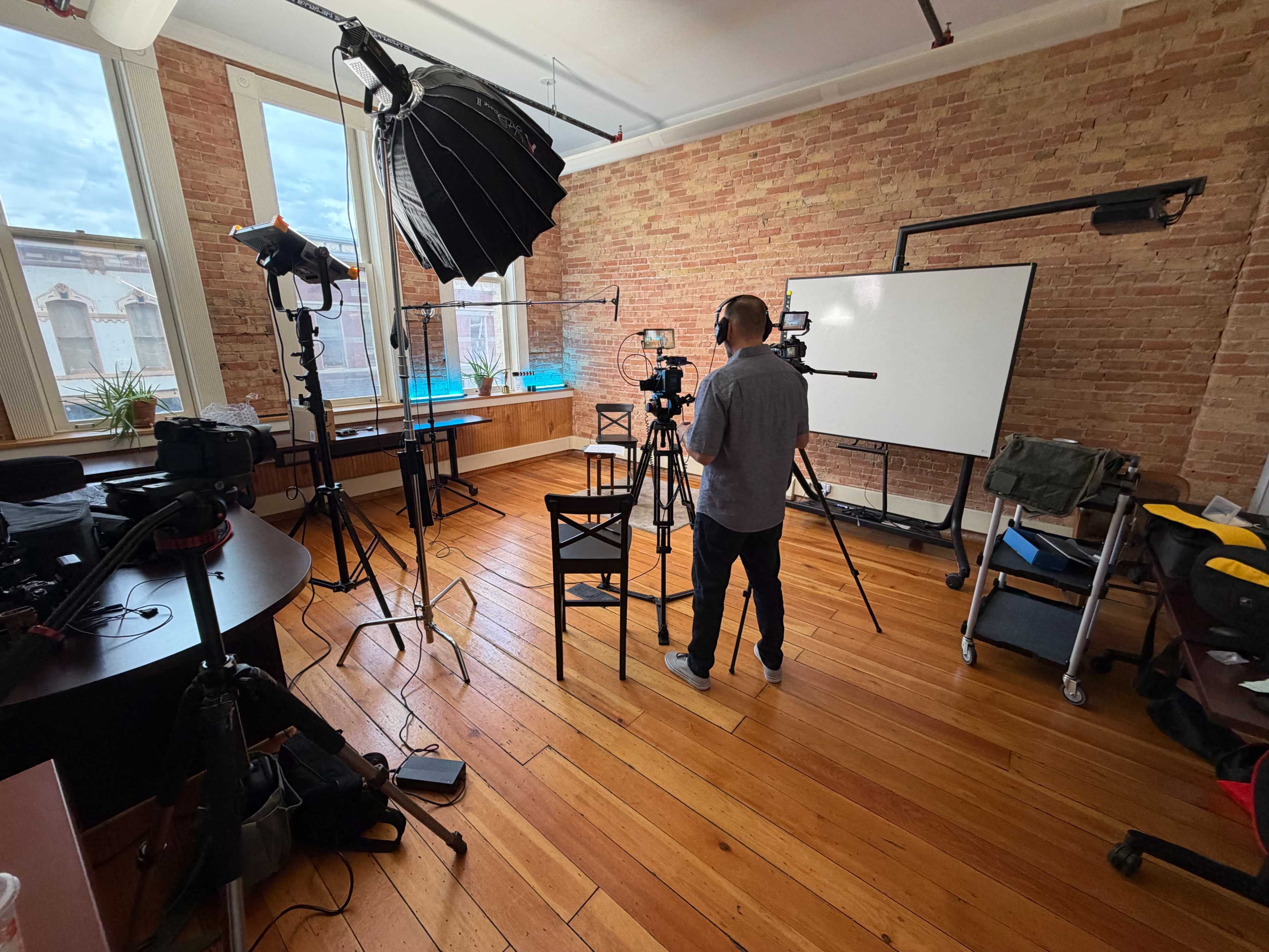 A man stands in a well-lit photography studio equipped with cameras, lighting, and staging equipment on wooden floors.