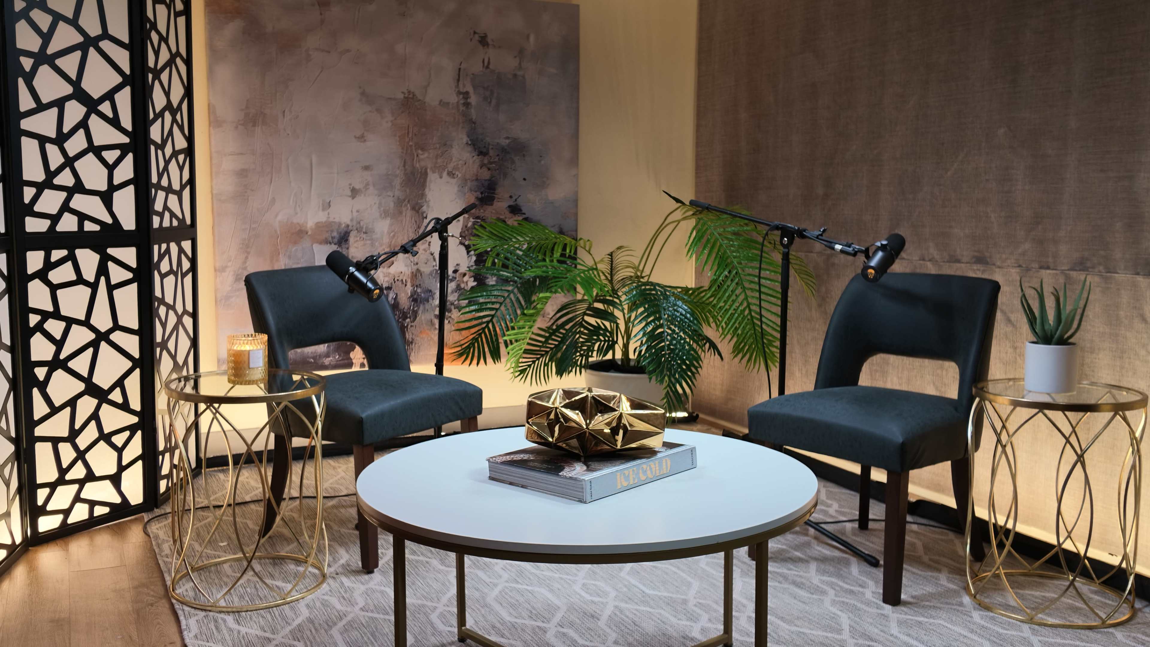 The image depicts a cozy interview setup with two chairs facing each other, a small round table adorned with decorative items, and soft lighting accentuated by plants in the background.