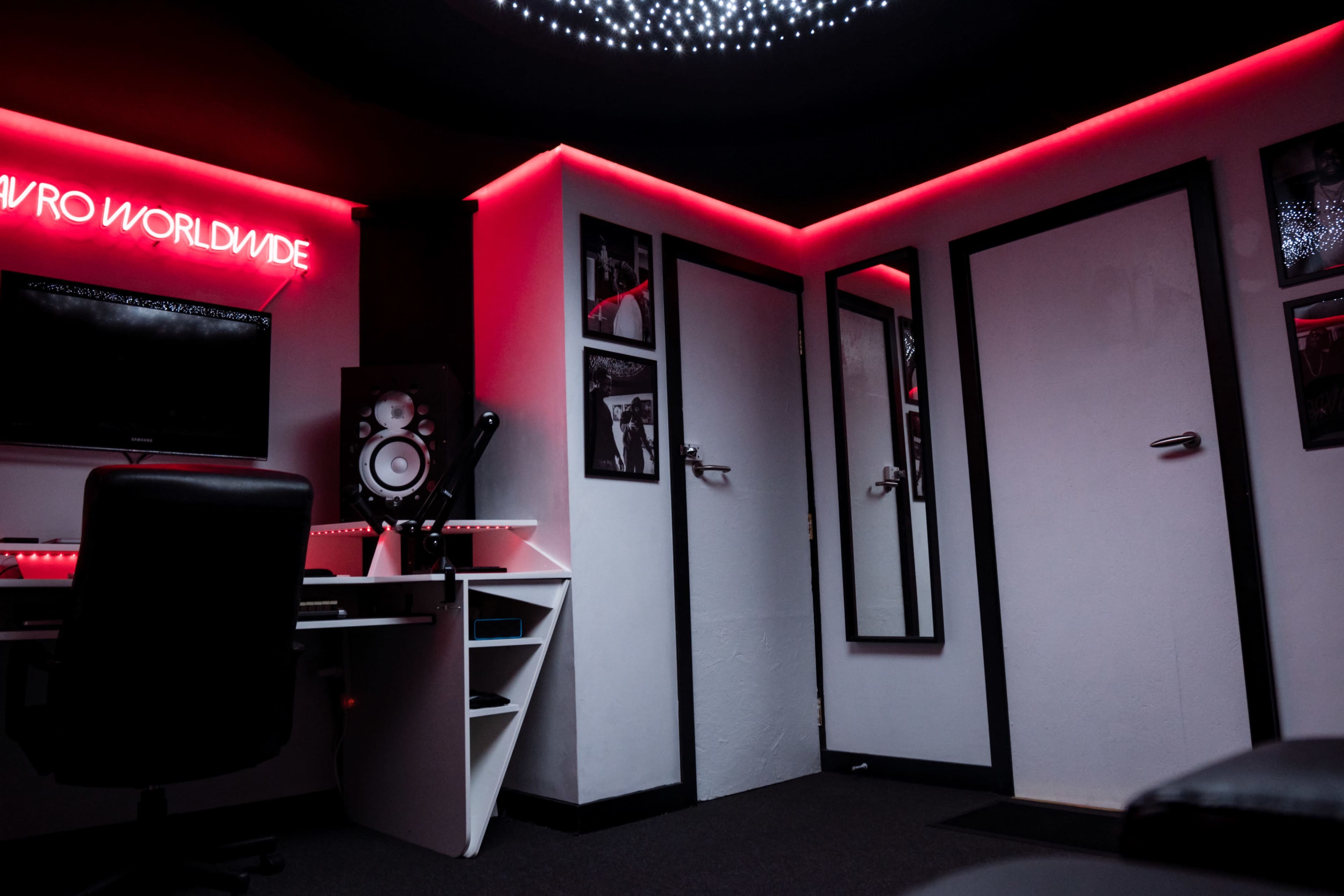 A dimly lit music studio with a computer setup, speakers, and illuminated walls.