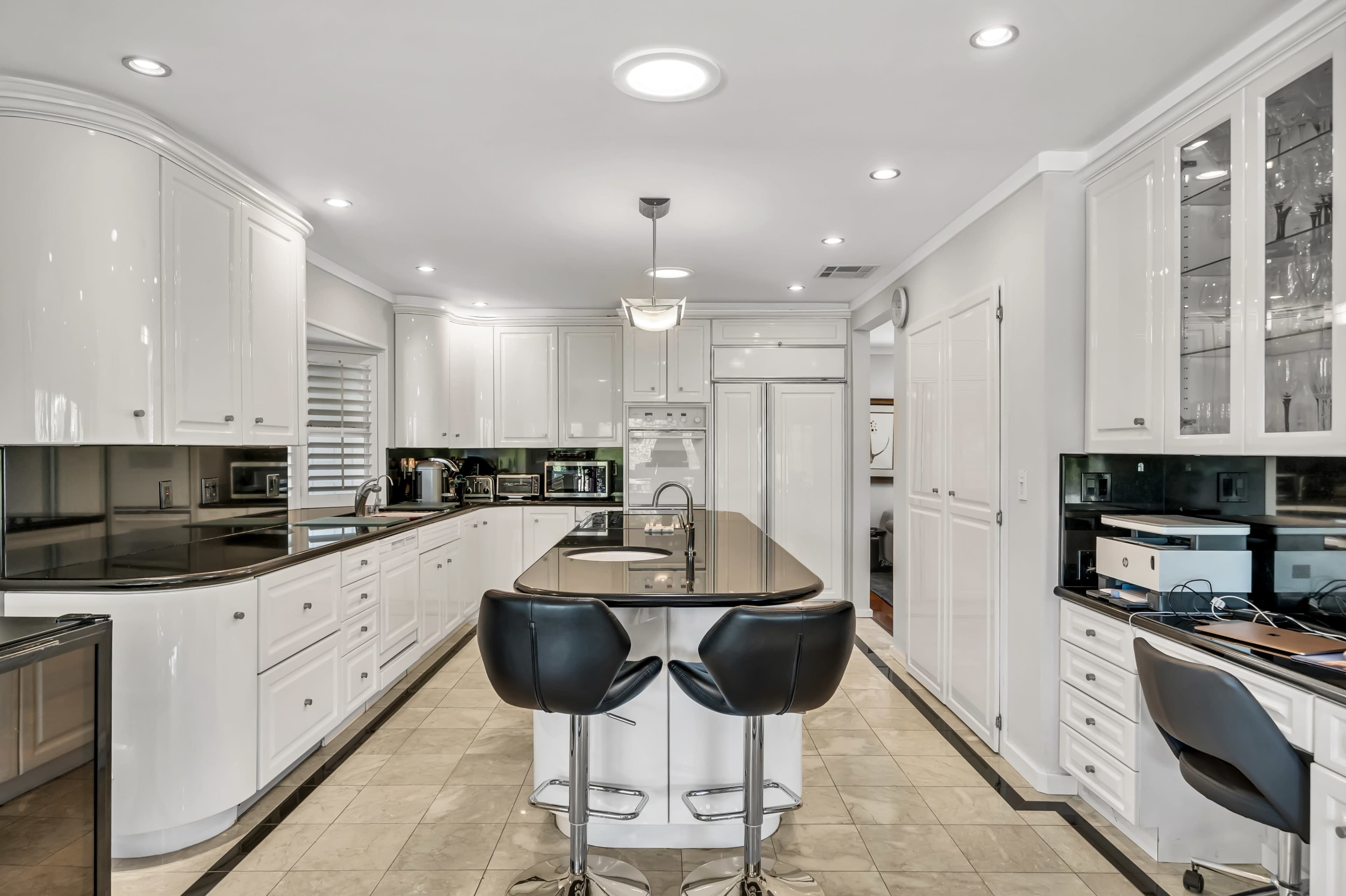 The image shows a modern kitchen featuring white cabinets, a black countertop island with circular bar stools, and stainless steel appliances.
