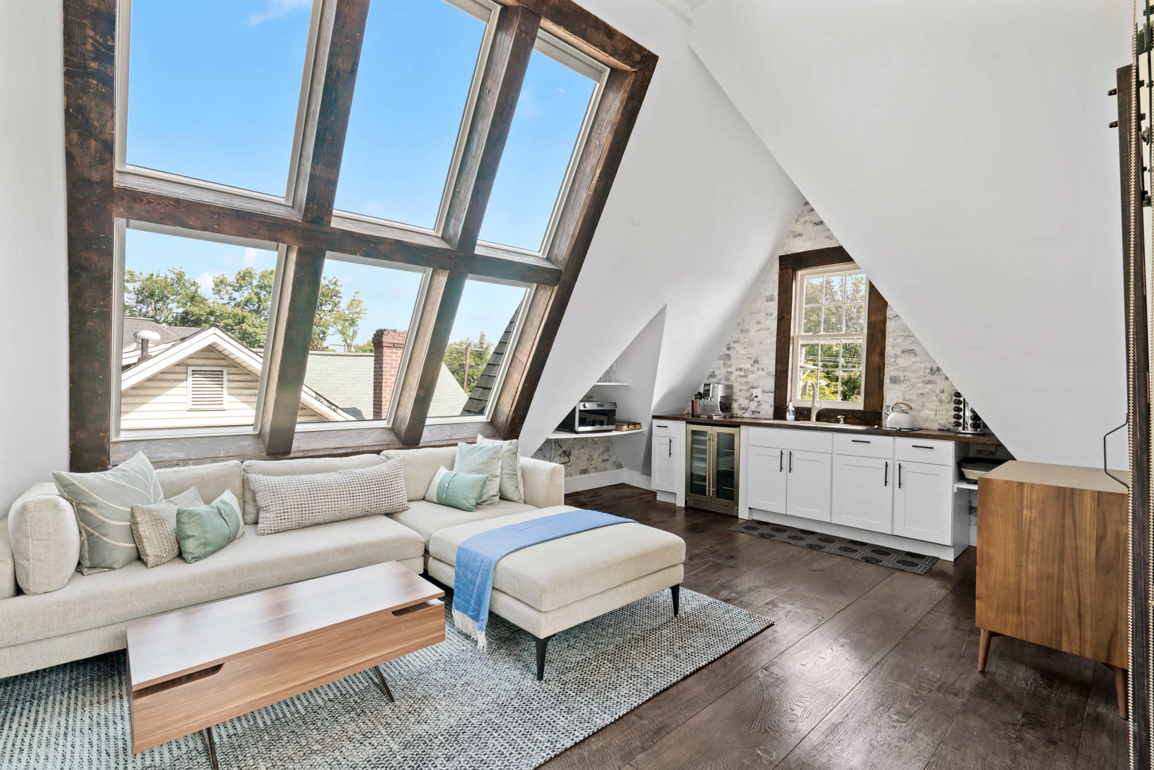 A modern living area with an abstract window design, a sectional sofa, and a kitchenette with wooden accents.
