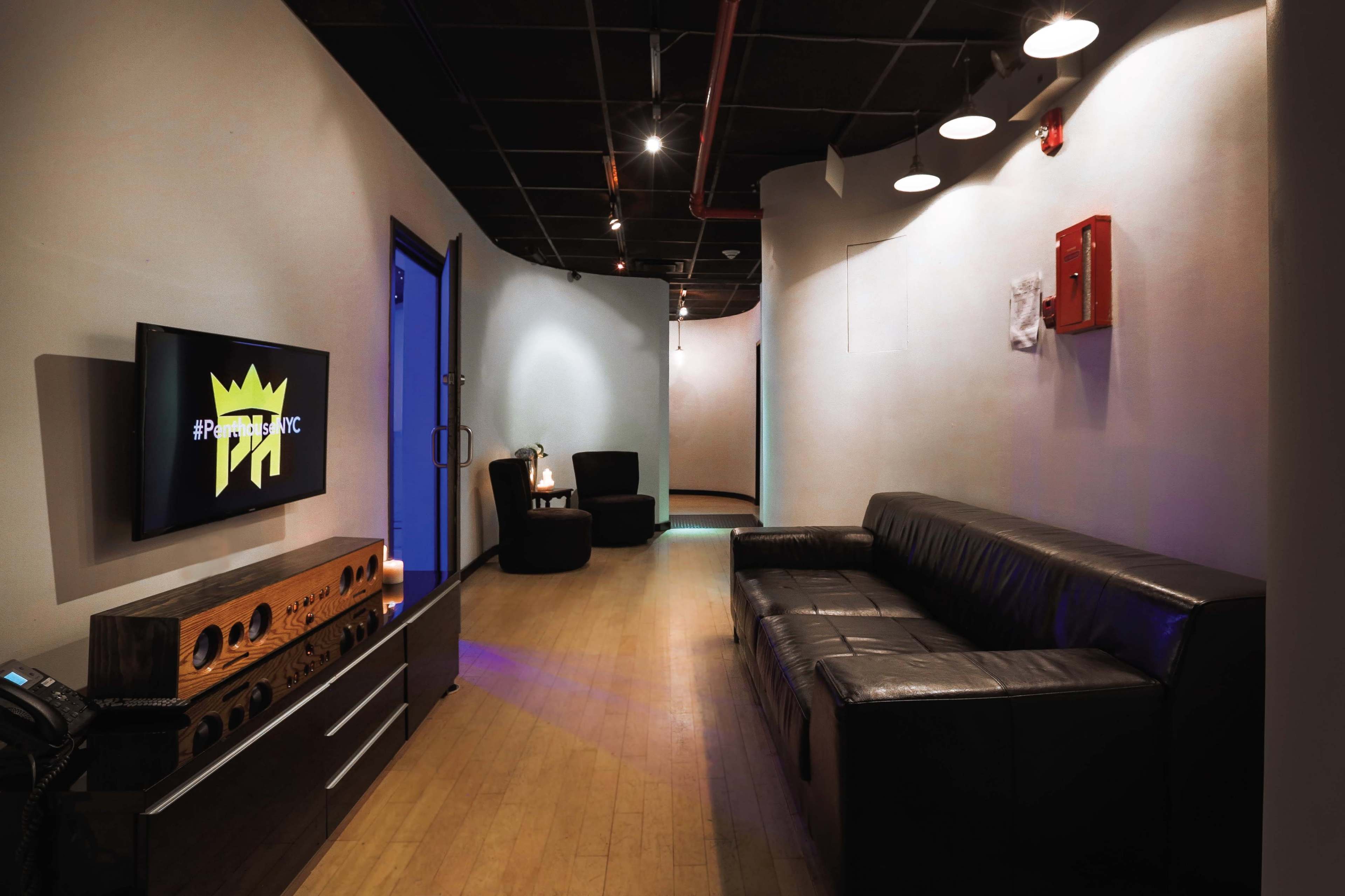 A sleek hallway features a black leather couch, a television mounted on the wall displaying a logo, and a modern wooden console table.