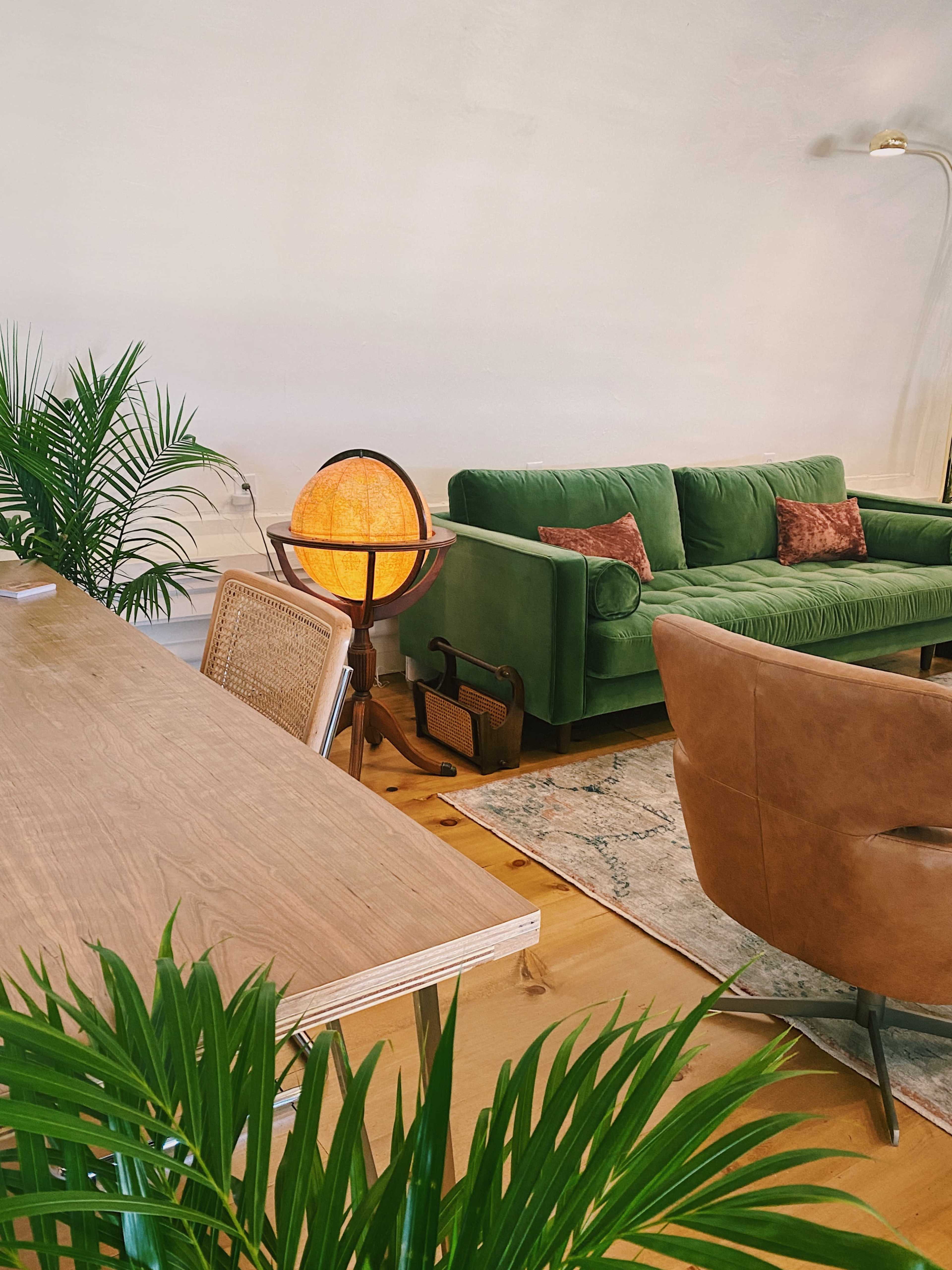 A modern living space featuring a green sofa, a wooden table, a globe lamp, and indoor plants.